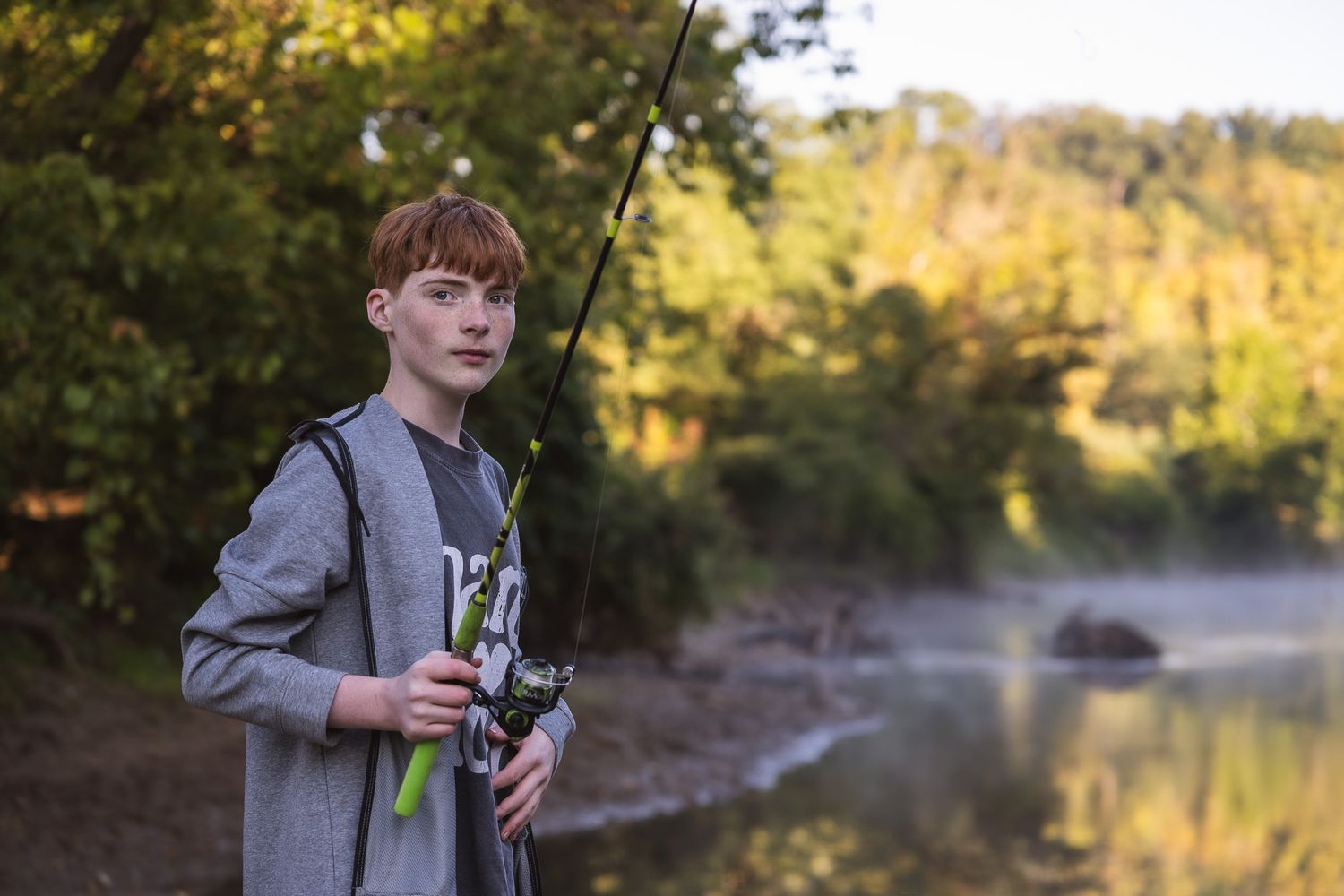 Young person fishing by a tranquil lake during golden hour.
