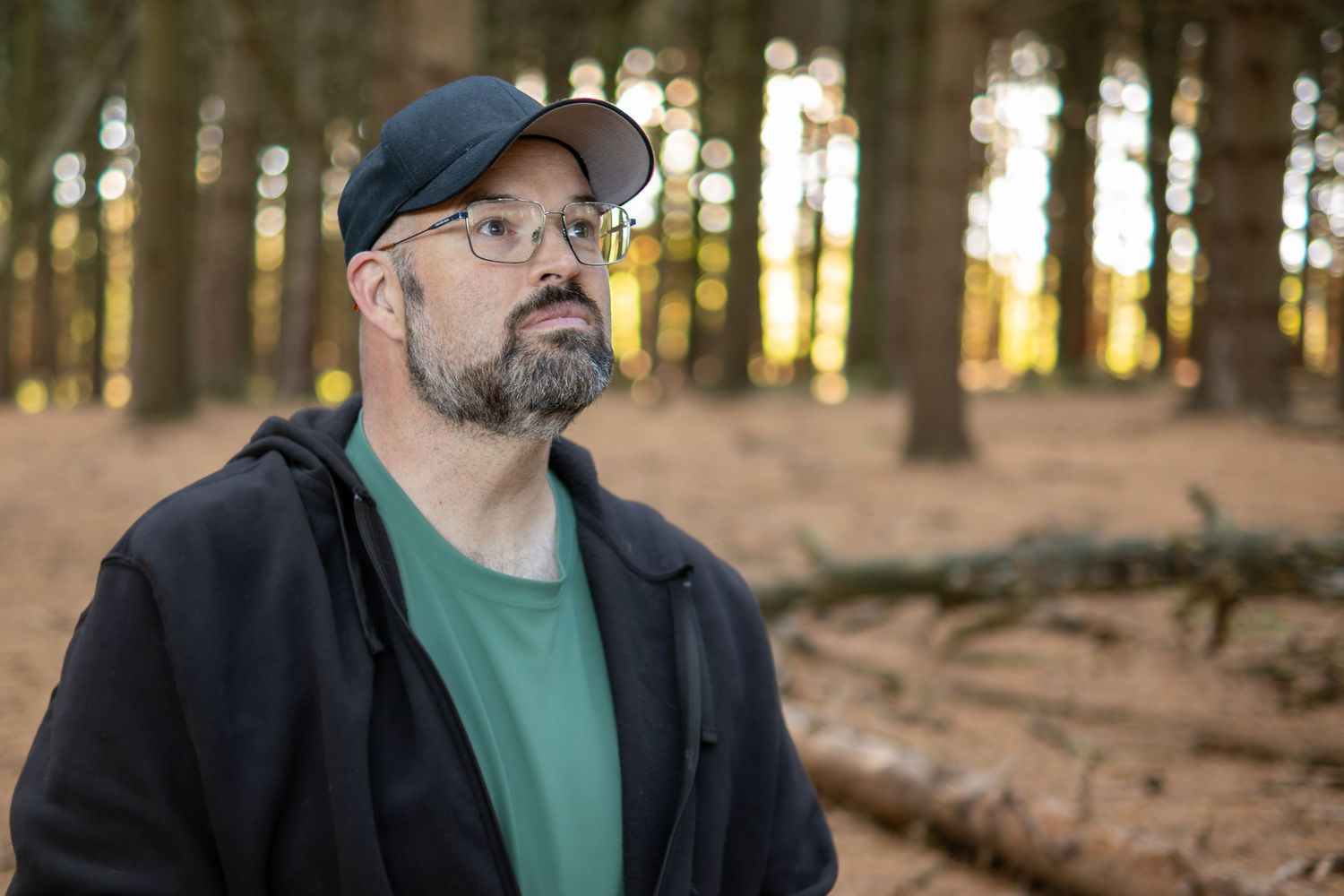 Person wearing a baseball cap walks through a sunlit forest path.