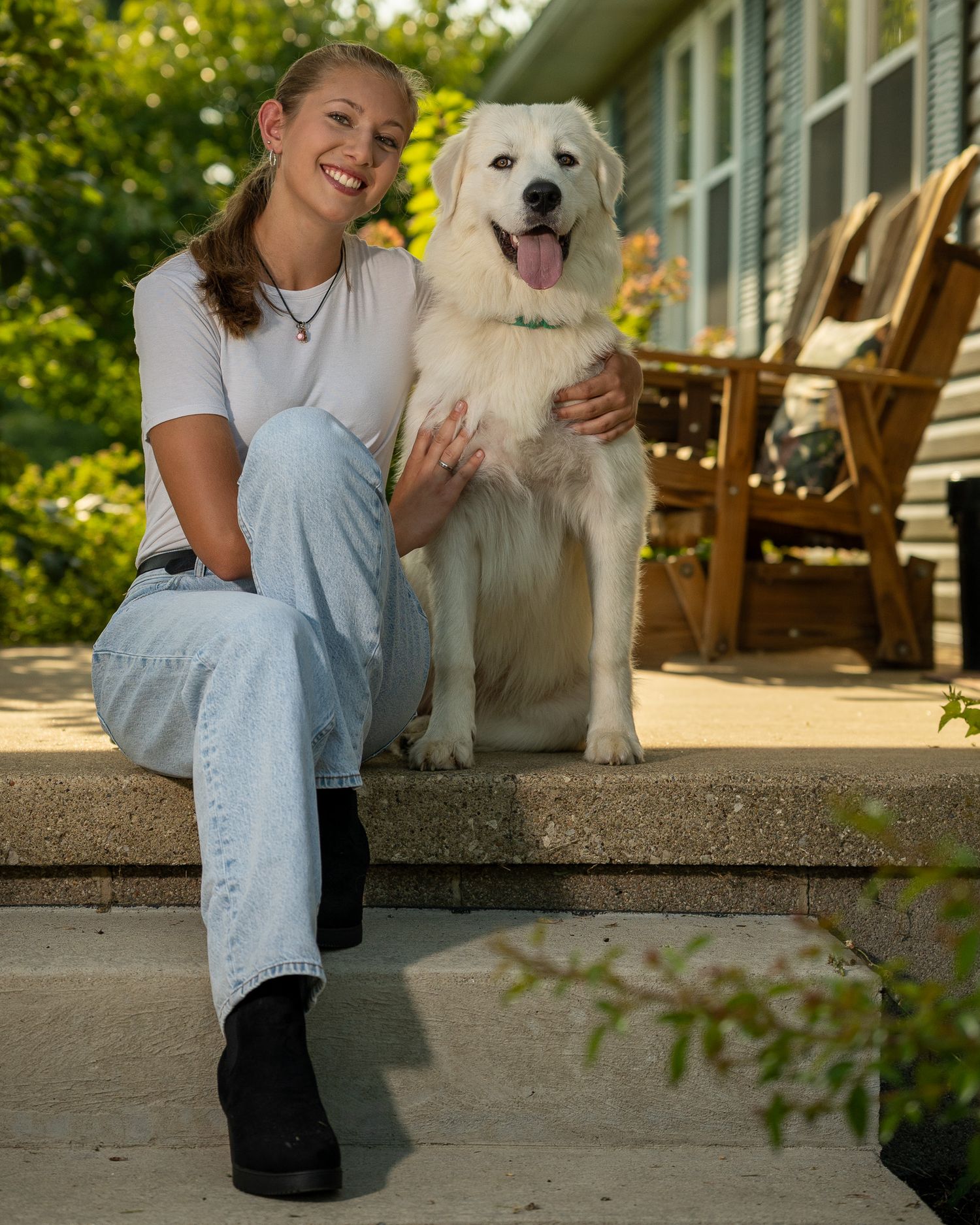 White dog and owner sitting together on outdoor porch steps in warm sunlight.