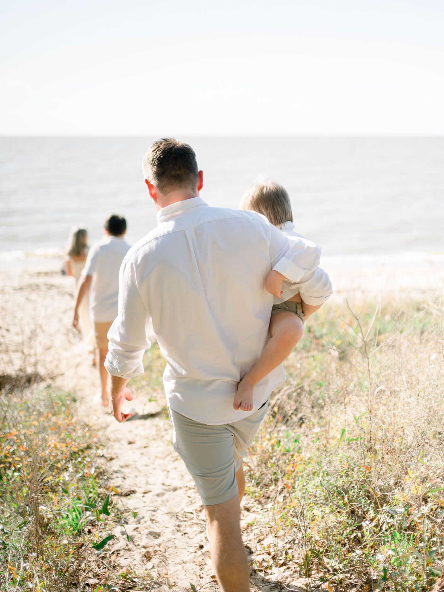 family walking down a sand path at Orange Street Pier beach in Fairhope Alabama during a golden hour photo session