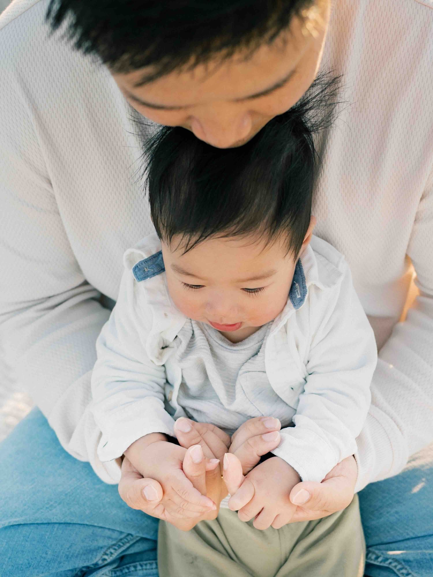 Dad and baby son sitting and holding hands during a sunrise family photography session in Dauphin Island, Alabama.Captured by AFV Photograpy