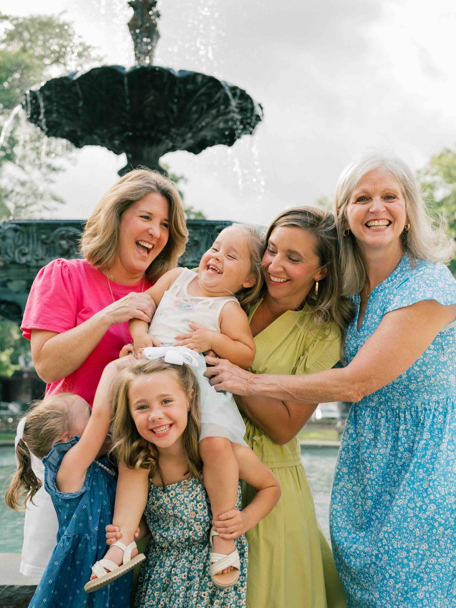 daughters, mother and grandmothers laughing and posing next to fountain at Bienville Square in Mobile Alabama