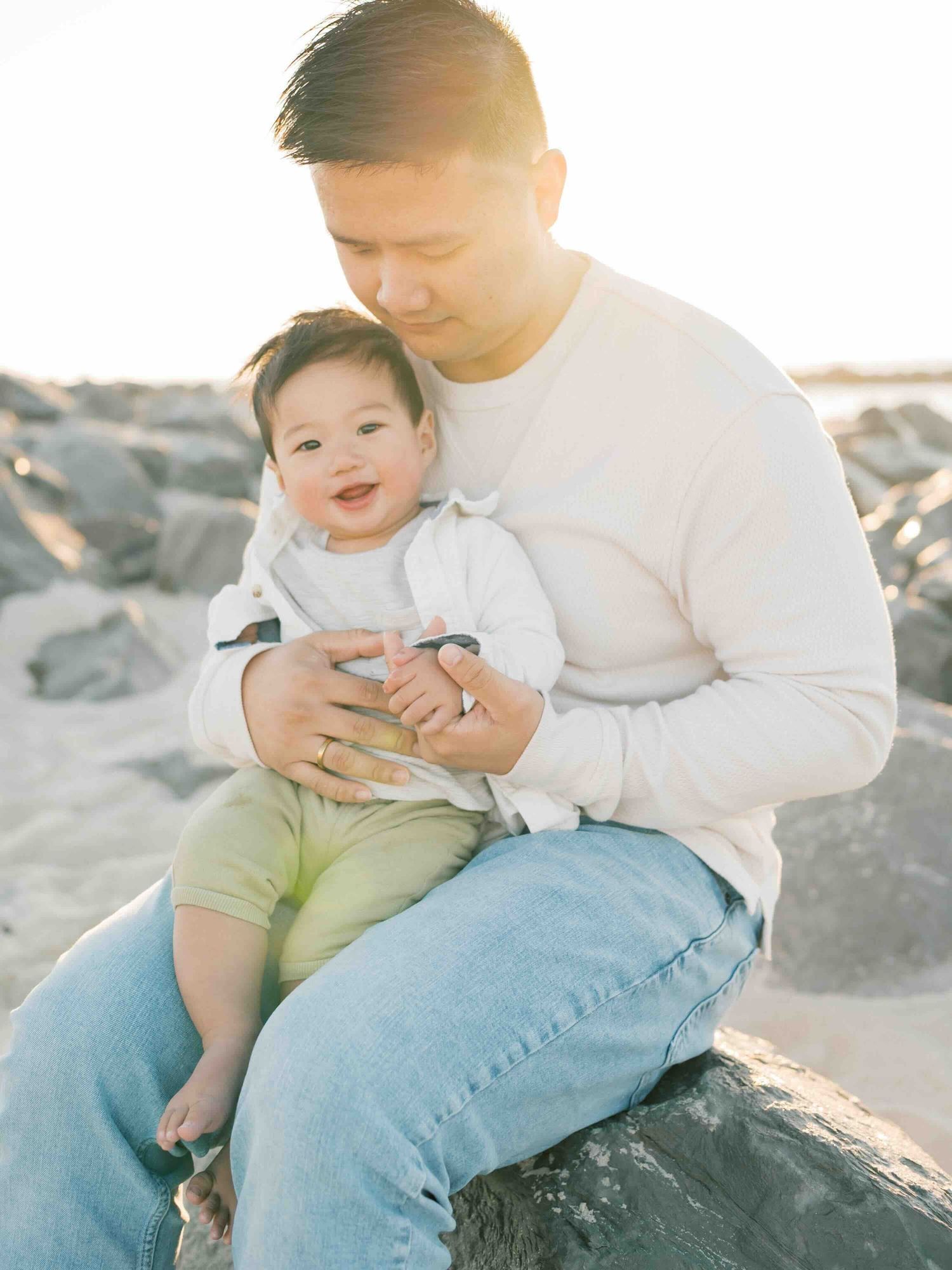 Dad and son sitting and cuddling during a sunrise family photography beach session on Dauphin Island captured by AFV Photography