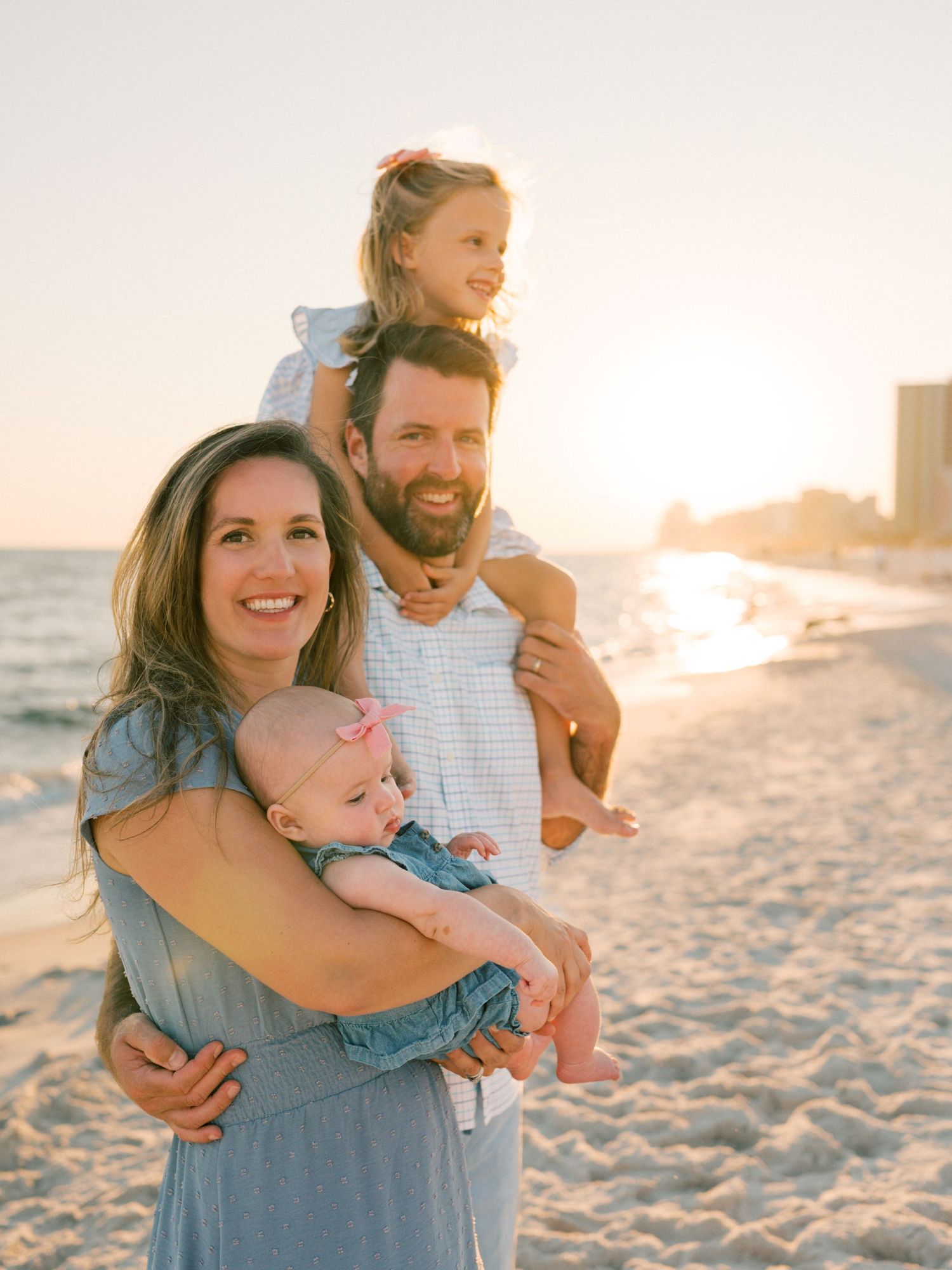 Family snuggling up along Orange beach waterline during golden hour photo shoot. Captured by AFV Photography.