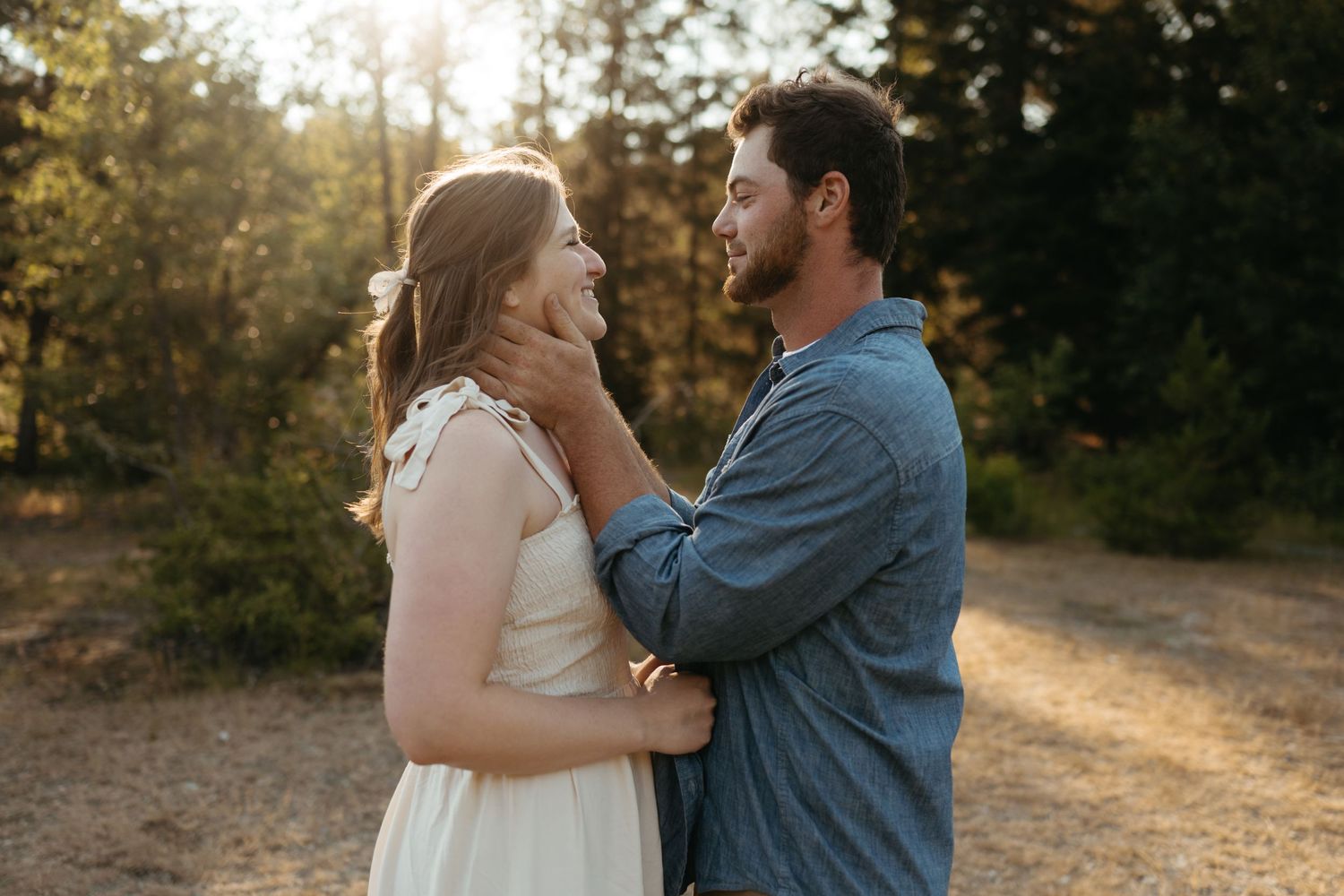 Tender moment between couple in casual clothes against sunlit forest background.