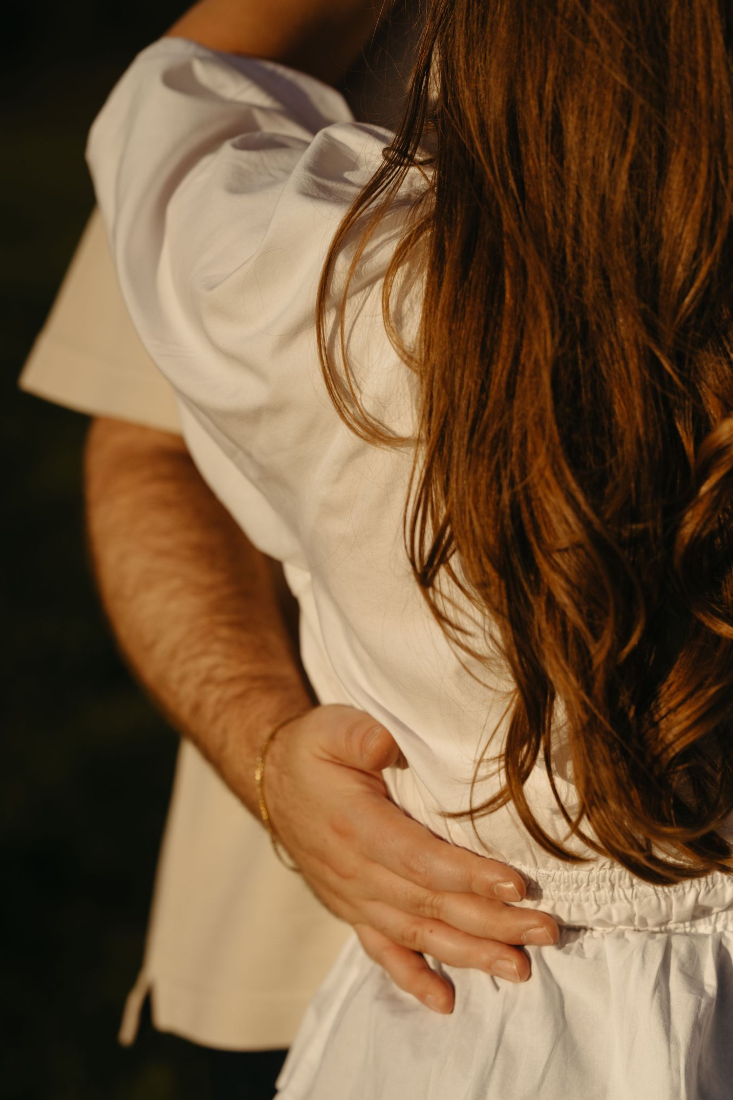 Intimate close-up of hands embracing against white clothing with long brown hair visible.