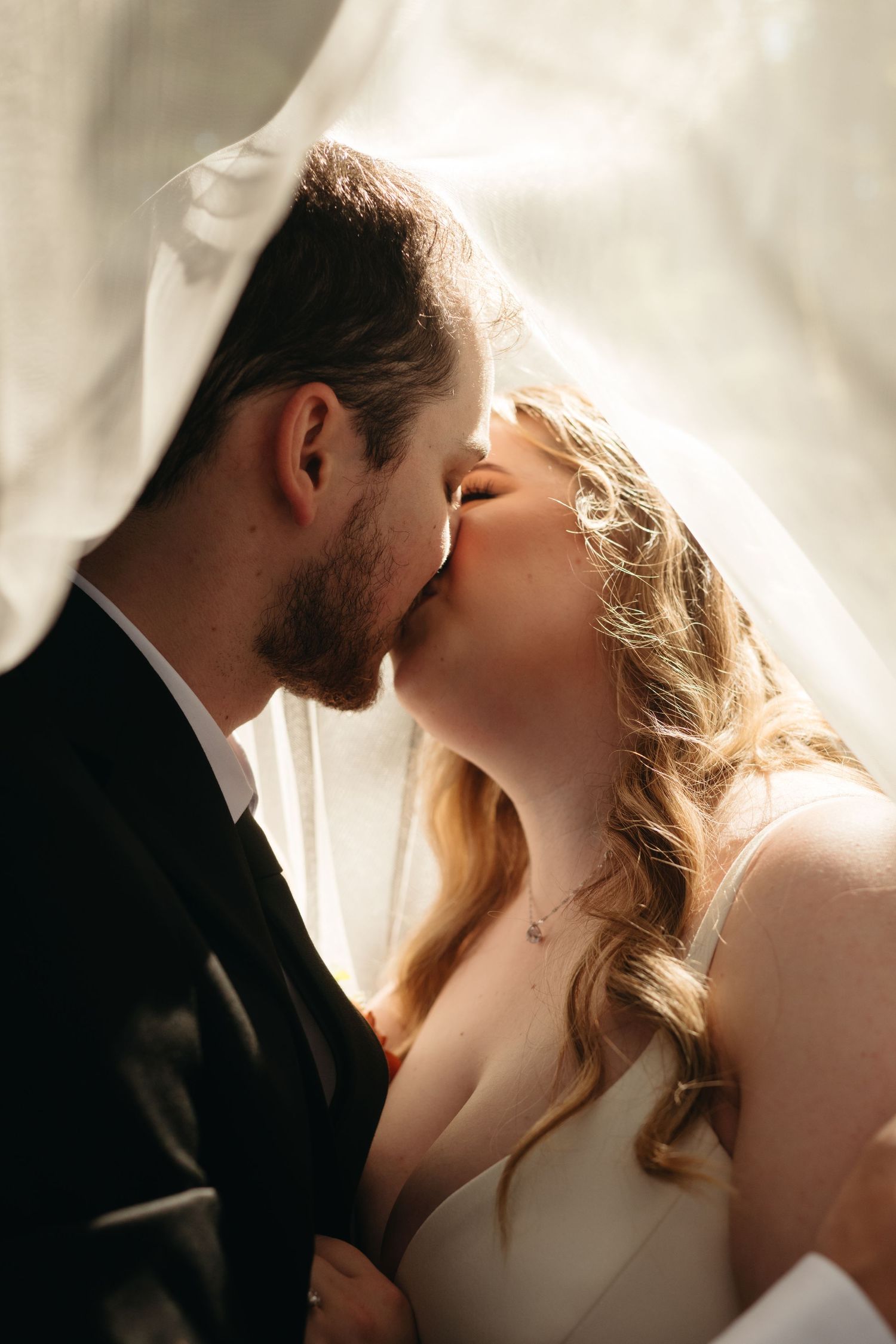 A tender kiss captured between newlyweds under a flowing white veil.