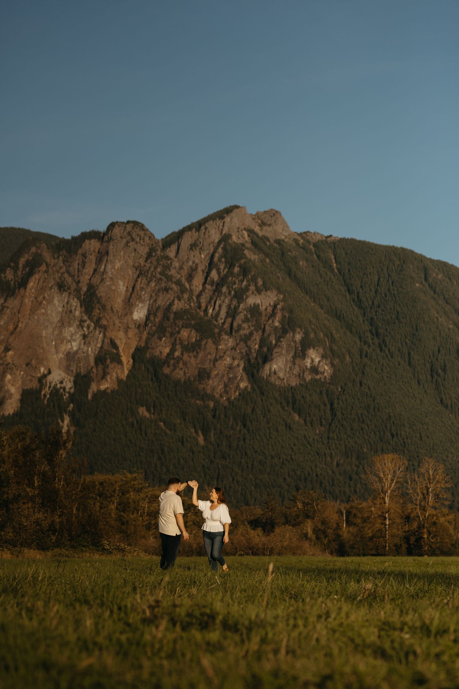 People holding hands while walking in grassy field with majestic mountain views.