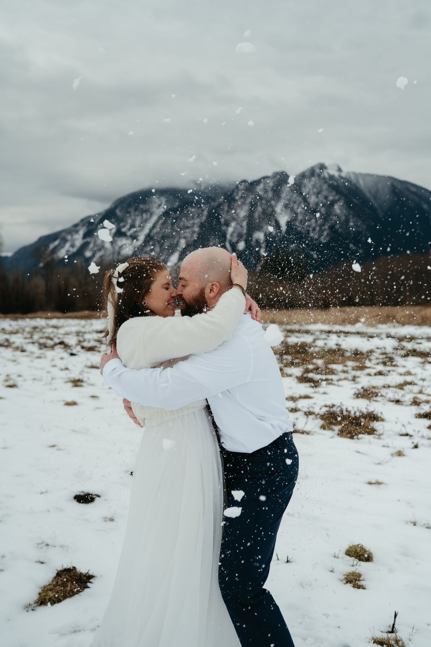 A couple shares a romantic moment in the snow with majestic mountains in the background.