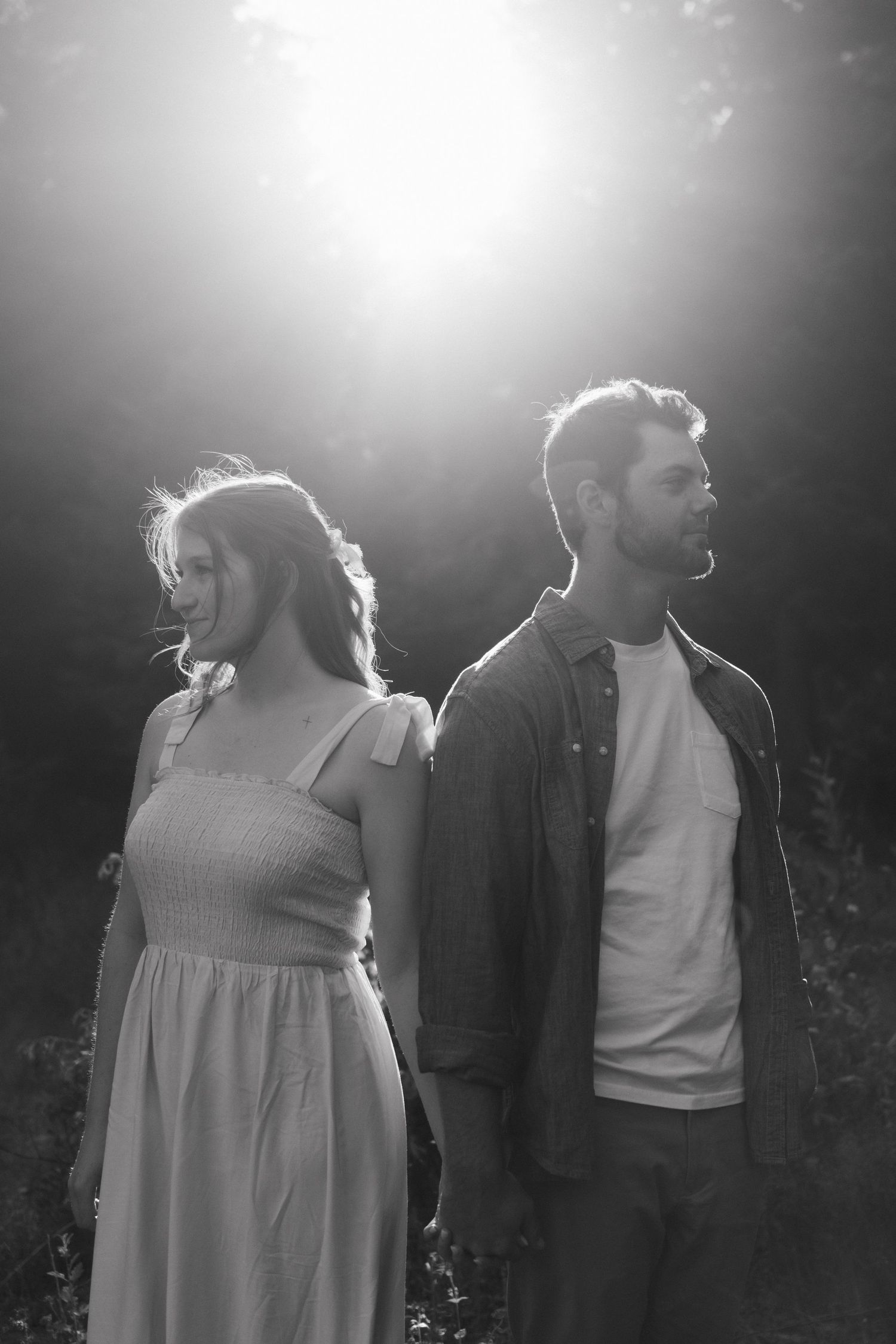 Artistic black and white portrait of a couple backlit by bright sunlight in a forest clearing.