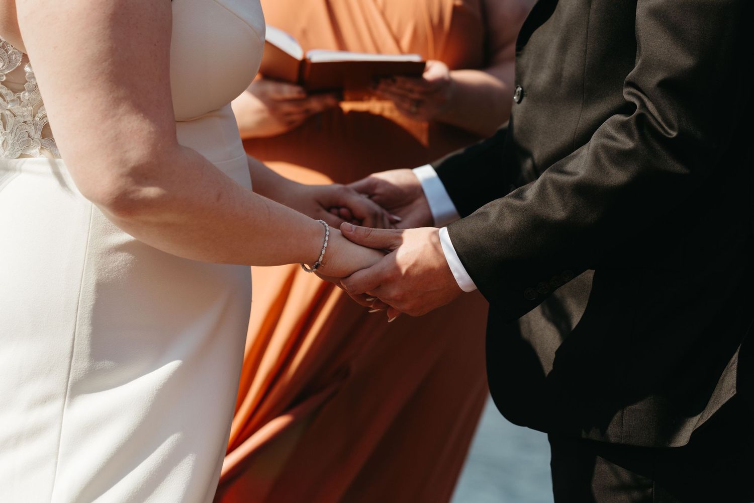 Close up of hands exchanging wedding rings against orange and white attire.