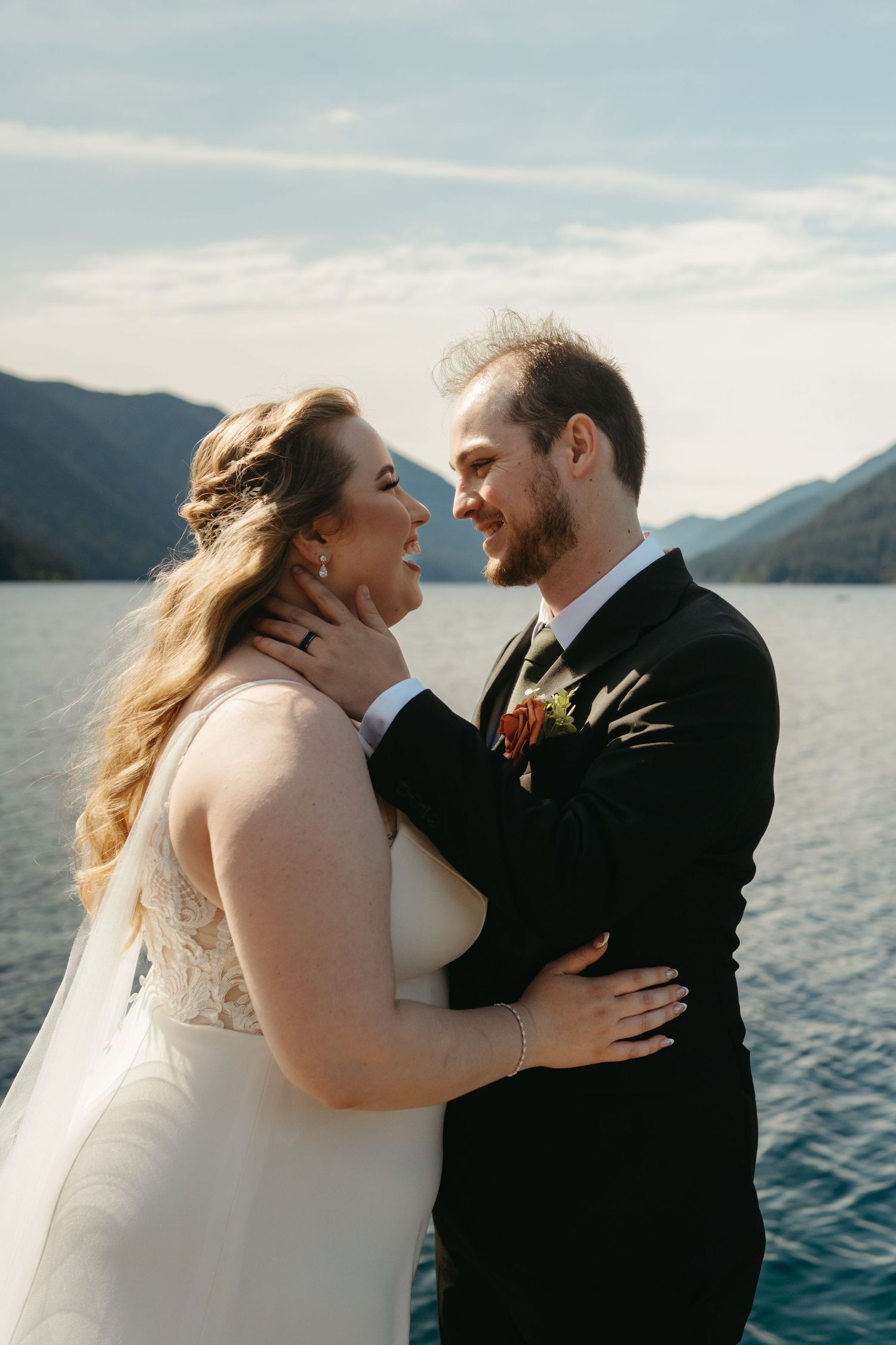 A romantic wedding portrait with a scenic mountain lake backdrop on a sunny day.