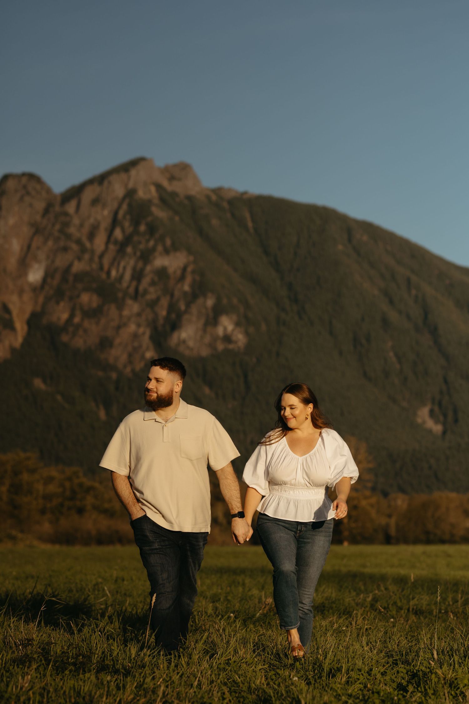 Couple walking through meadow with towering mountain peaks in warm sunset light.