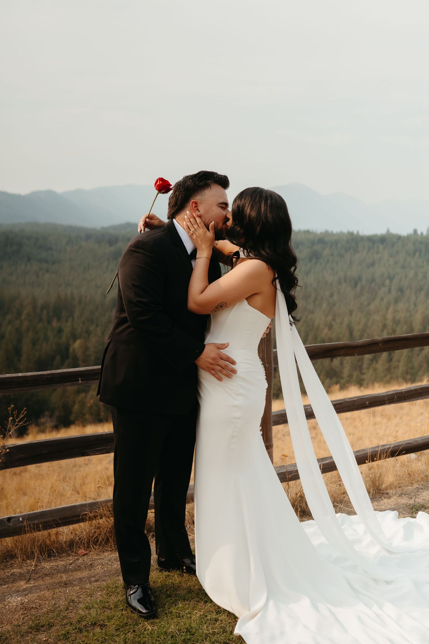A wedding couple shares a romantic kiss against a mountain backdrop at sunset.