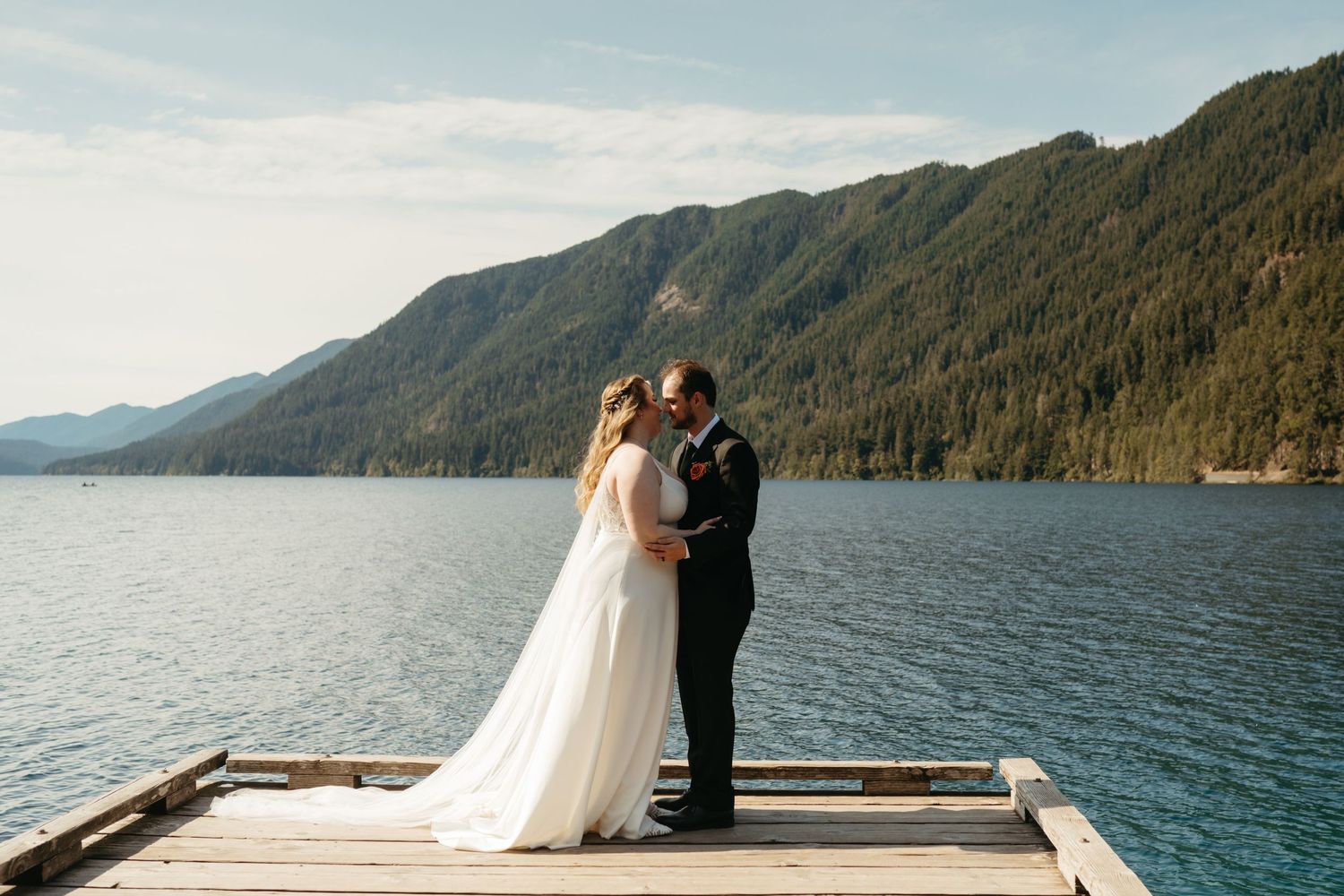 Newlyweds share an intimate moment on a wooden dock overlooking a pristine mountain lake.