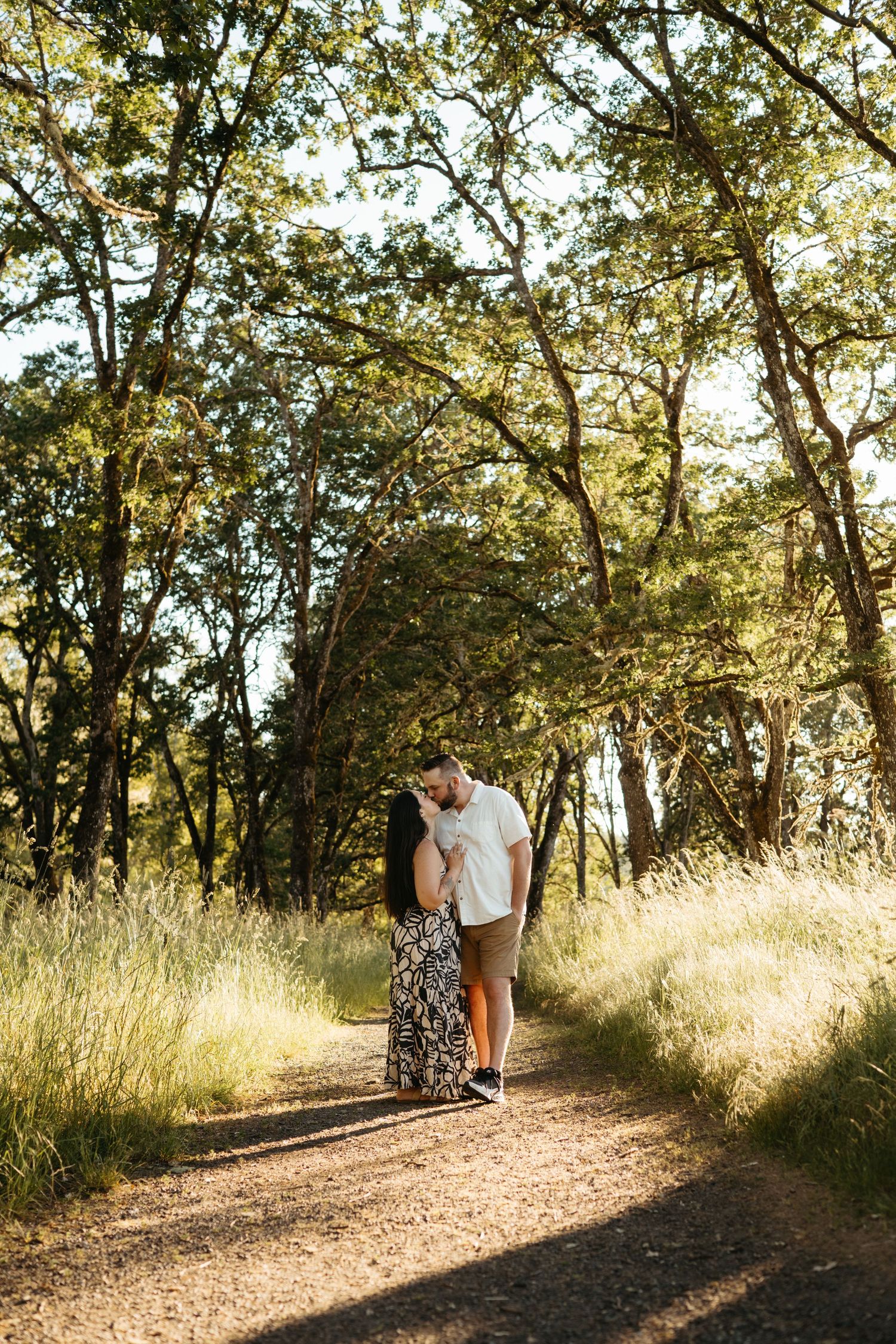 A romantic couple walks along a sunlit forest trail surrounded by golden trees.