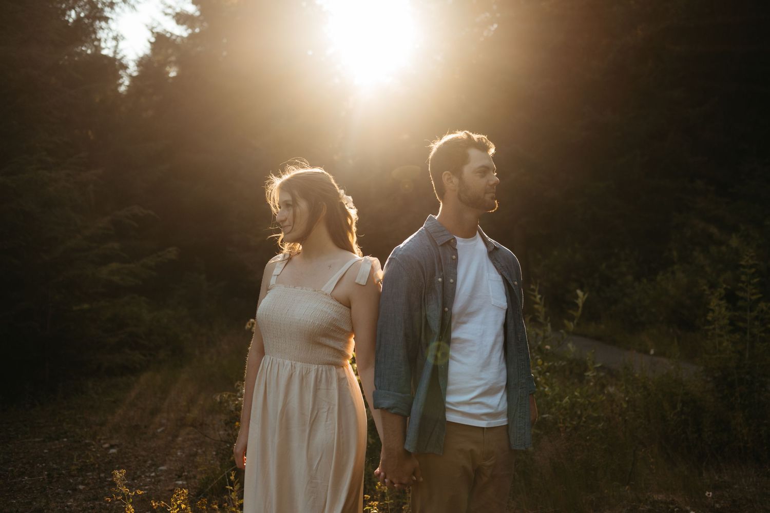 Backlit couple standing in golden sunlight with evergreen forest behind them.