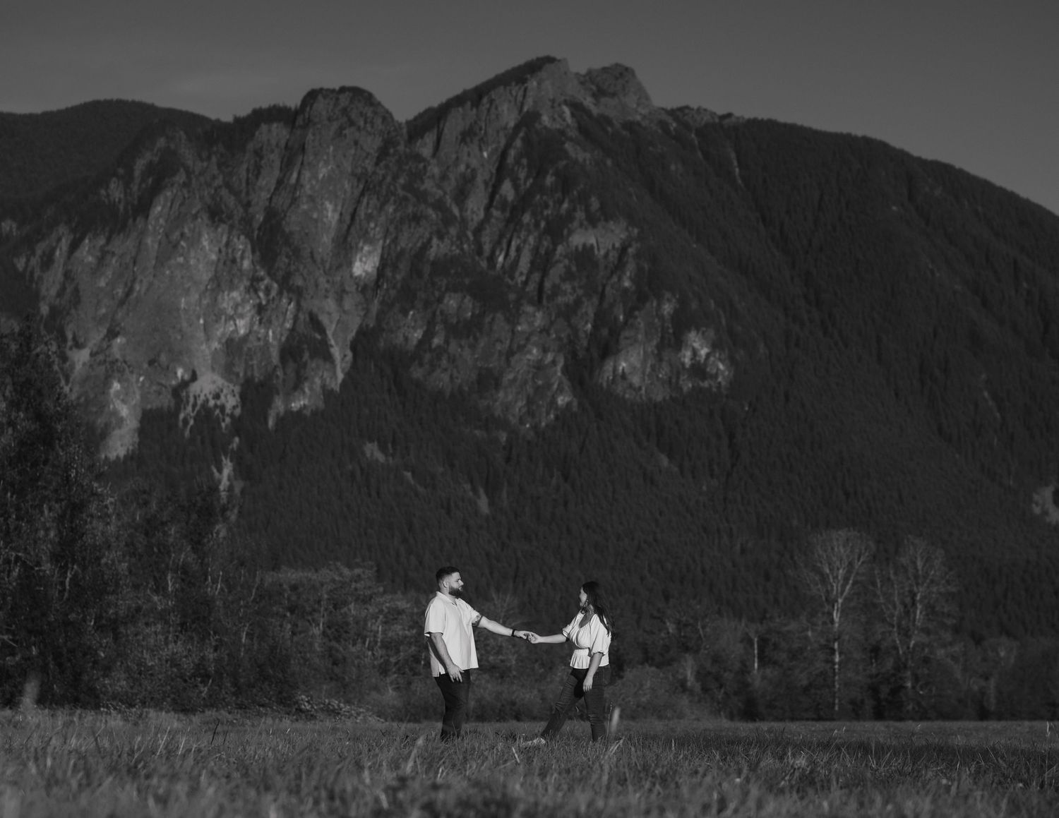 Black and white photo of figures dancing in field with mountain landscape.