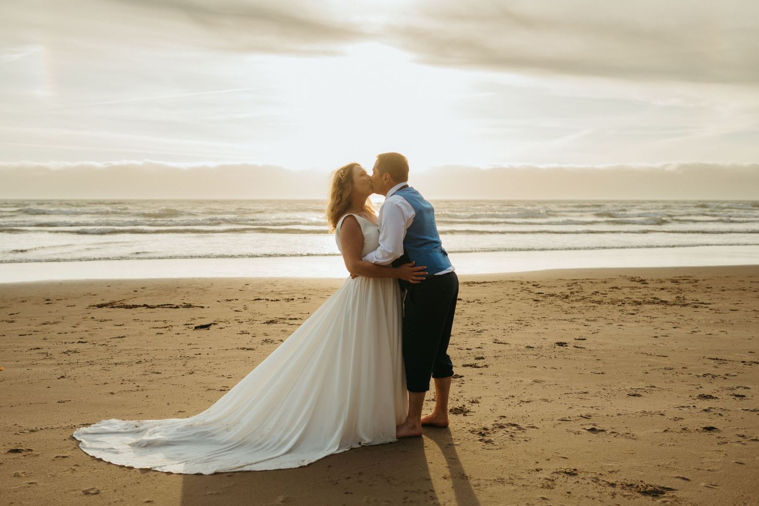 Romantic beach wedding photo during golden hour sunset with flowing white dress.