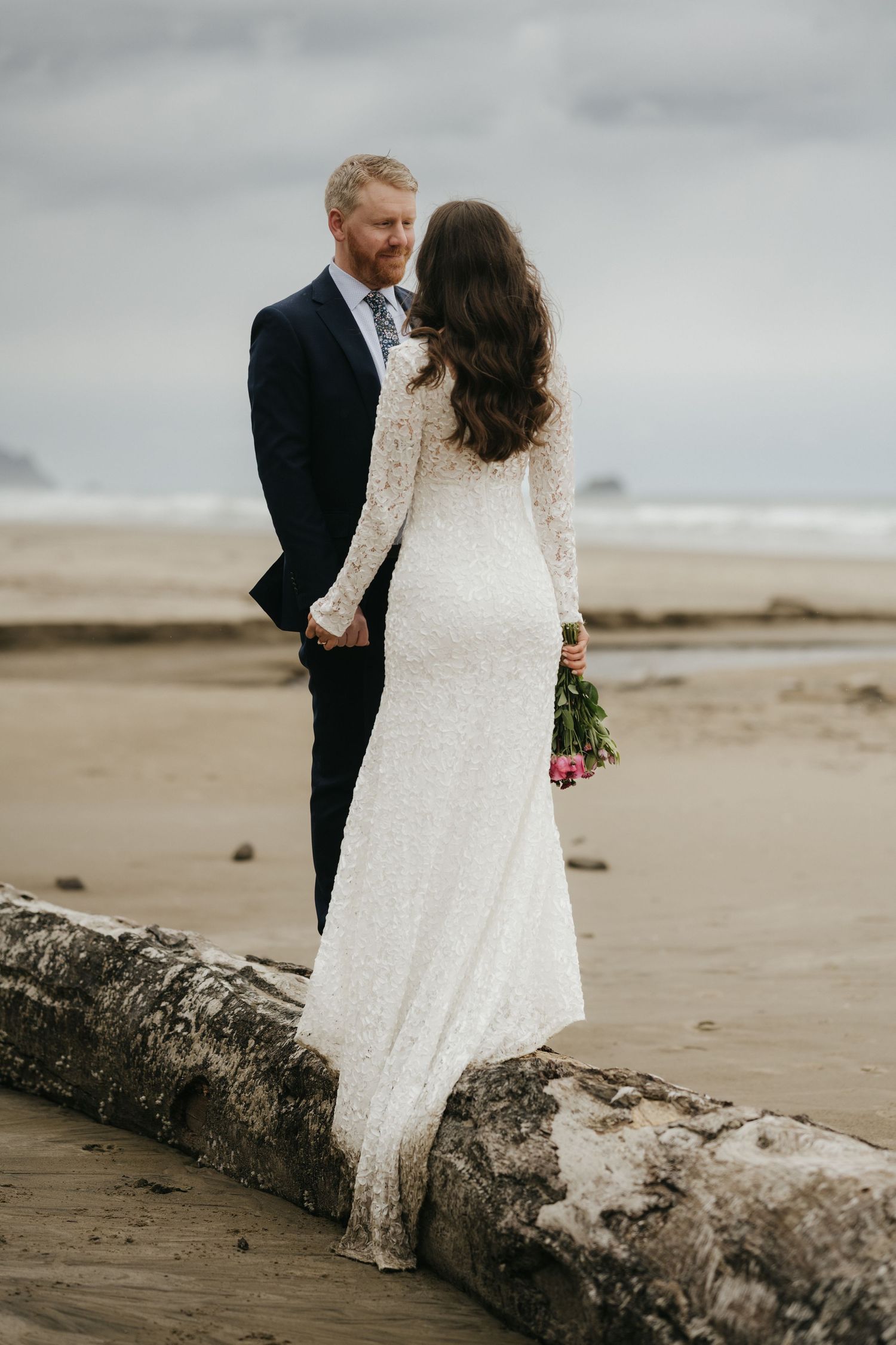 A couple sharing a tender moment while standing on driftwood at the beach.