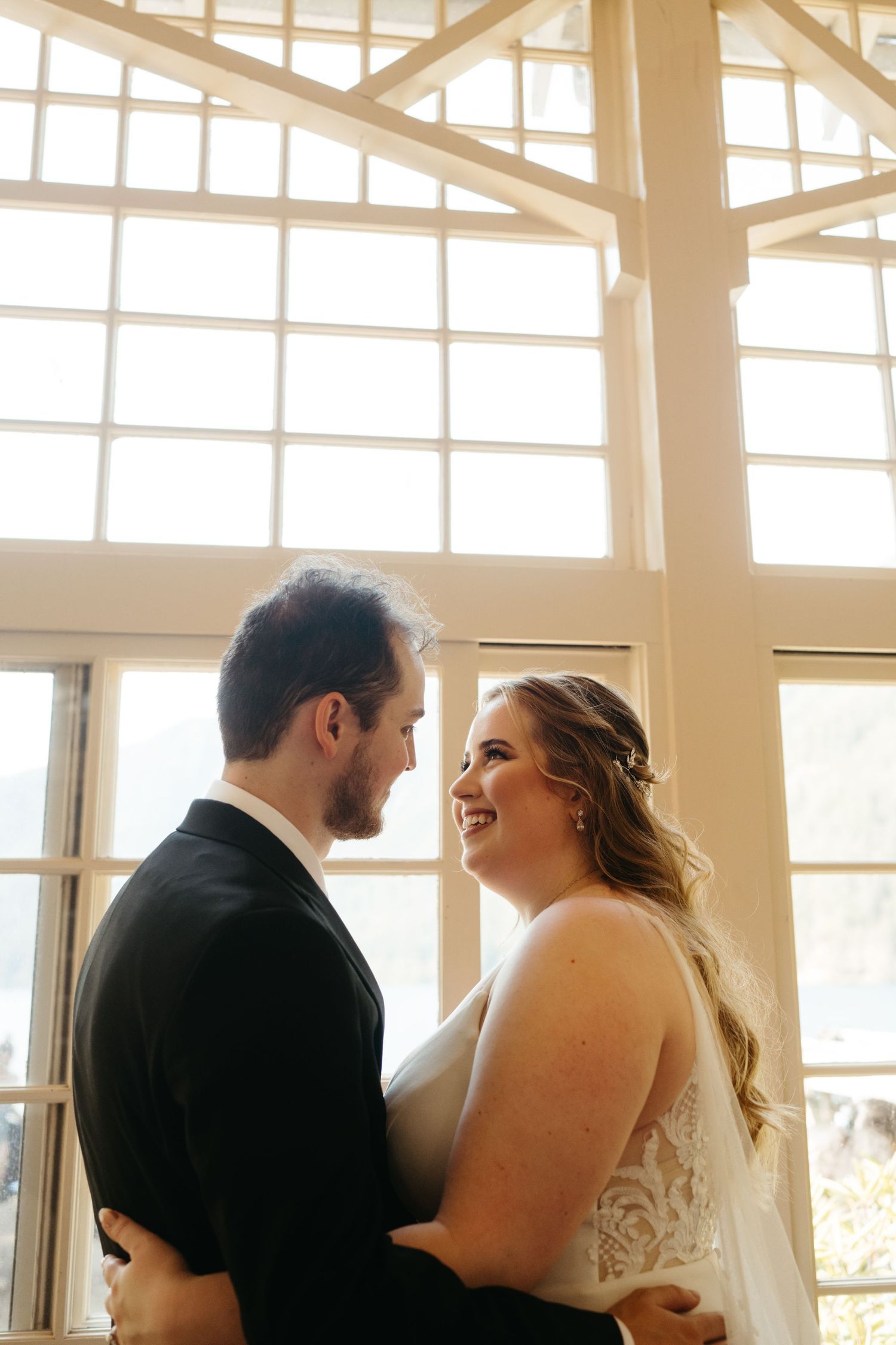 A joyful wedding moment captured in a bright sunlit room with large windows and wooden beams.