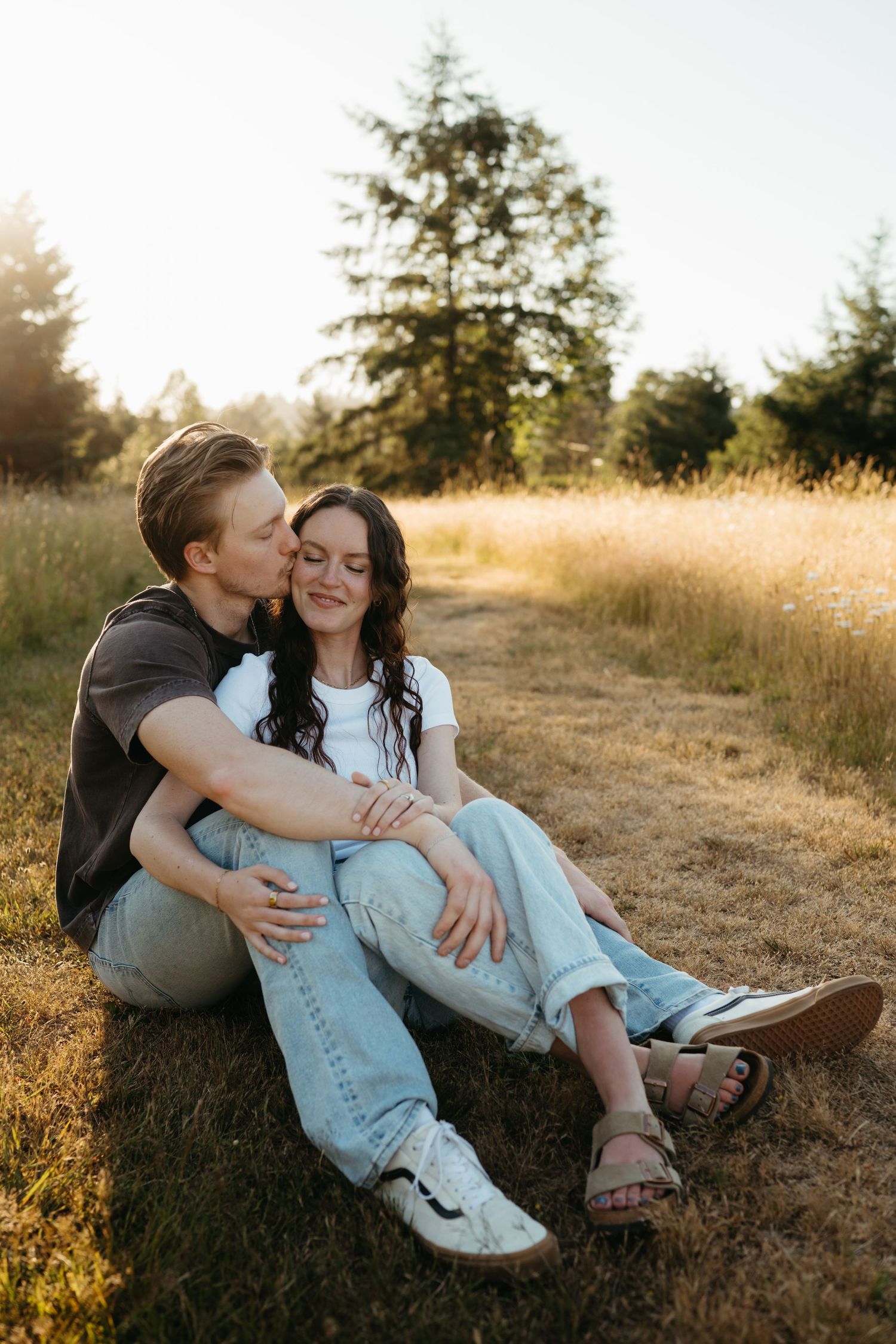 Couple sitting in golden meadow at sunset, man kissing womans cheek.