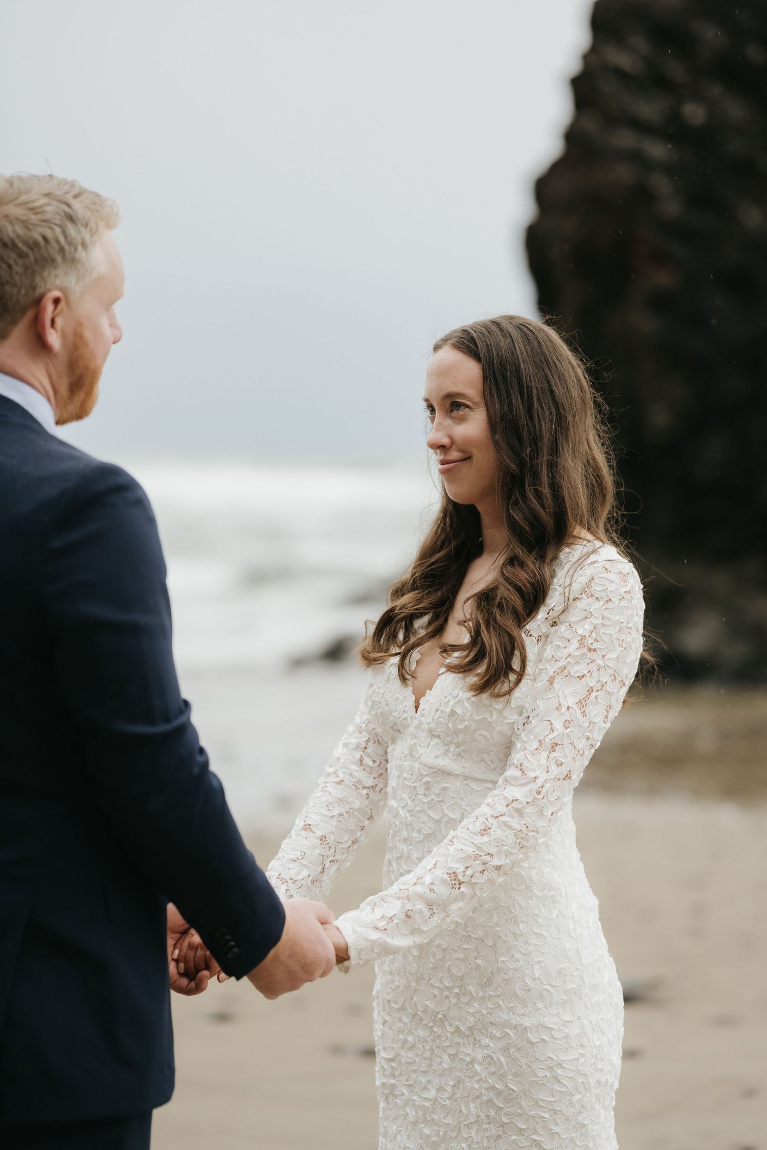 A couple shares an intimate moment during their wedding ceremony on a misty beach with cliffs.