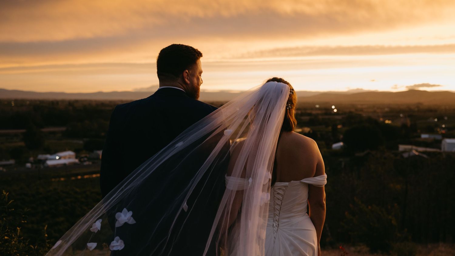 Silhouetted figures against vibrant orange sunset sky at coastal location.