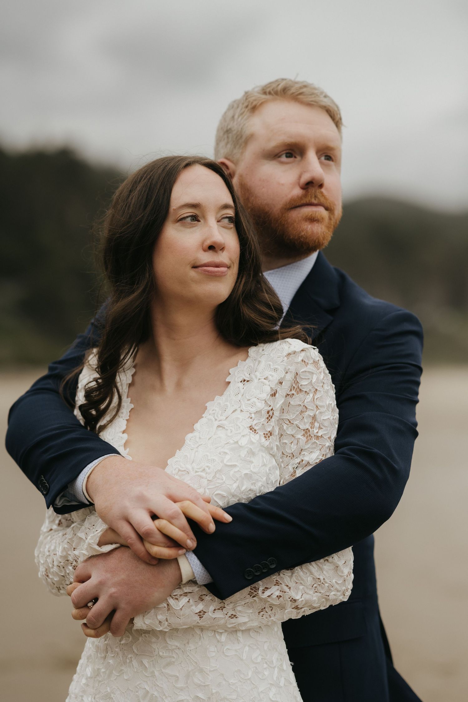 Intimate portrait of newlyweds embracing on a cloudy beach.