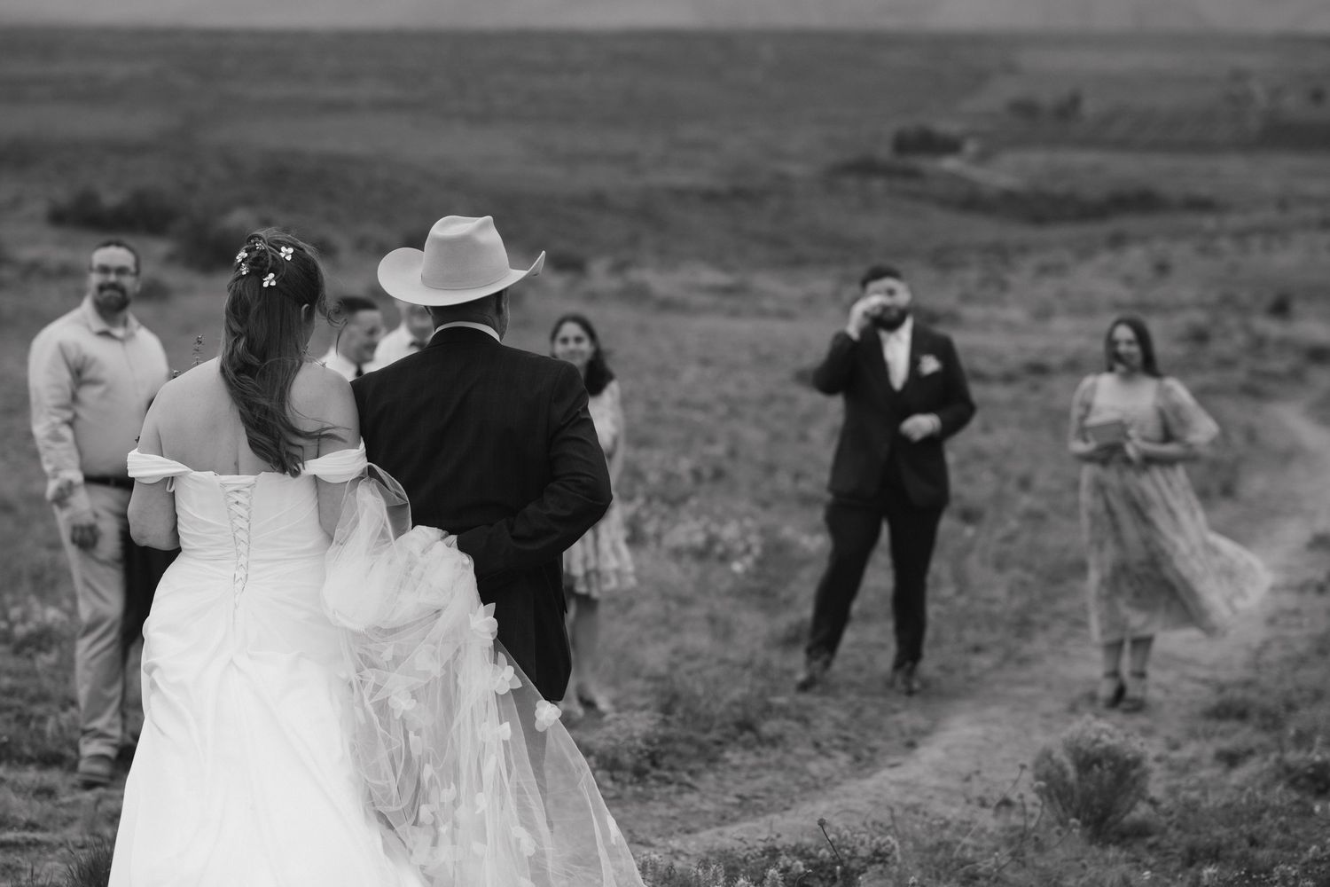 Wedding party gathers on hillside for candid black and white photo.