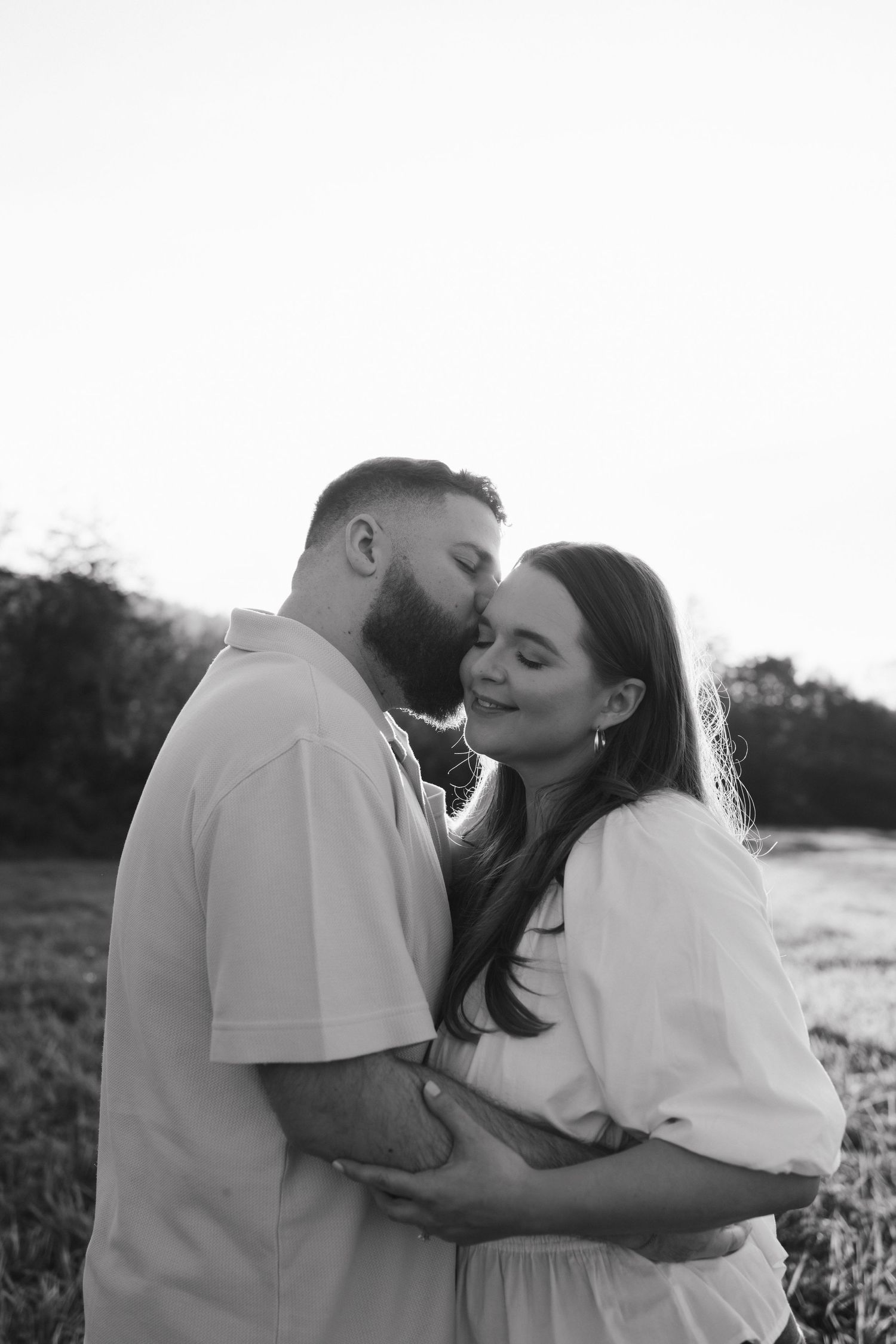 Black and white intimate portrait of couple in white clothing embracing outdoors.
