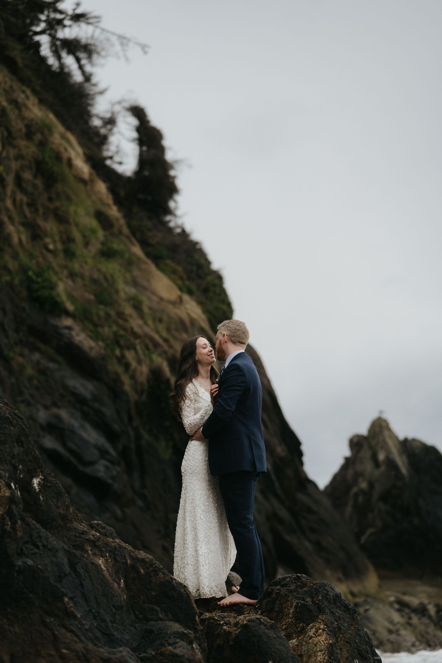 A romantic moment captured between newlyweds standing on rocky coastal cliffs.