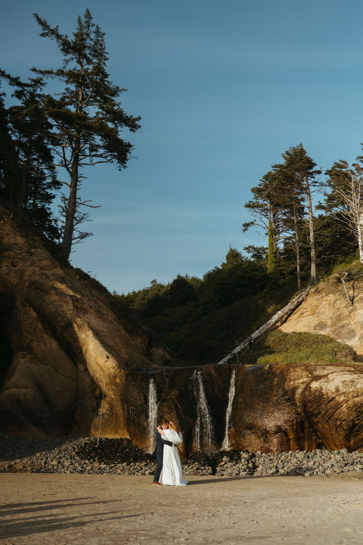 Couple walking on sandy beach with towering coastal cliffs behind them.
