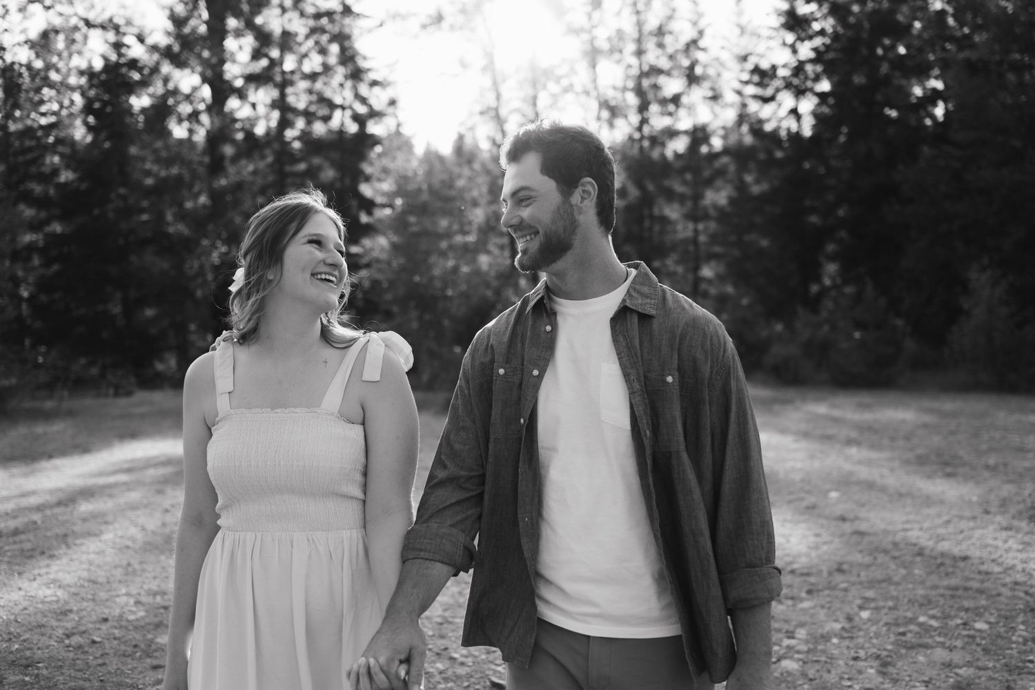A couple shares a joyful moment while walking together on a dirt path in black and white.
