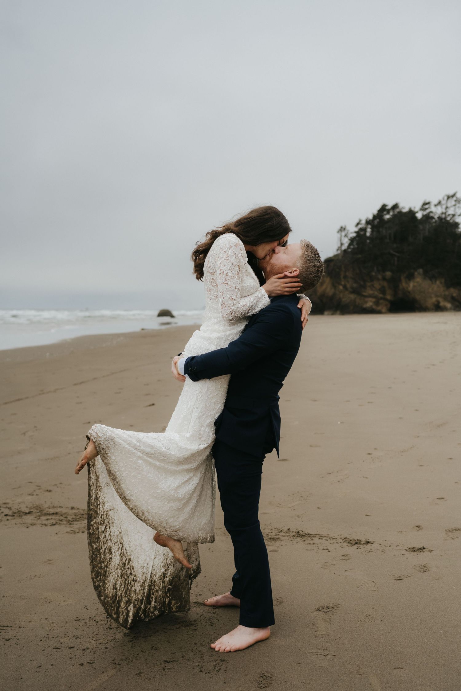 Romantic embrace on misty beach with coastal cliffs in background.