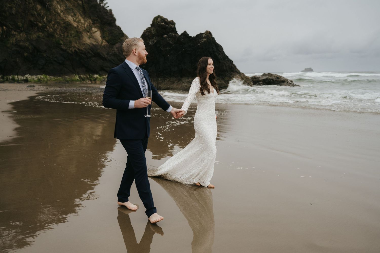 Couple walking along misty beach shoreline during coastal wedding celebration.