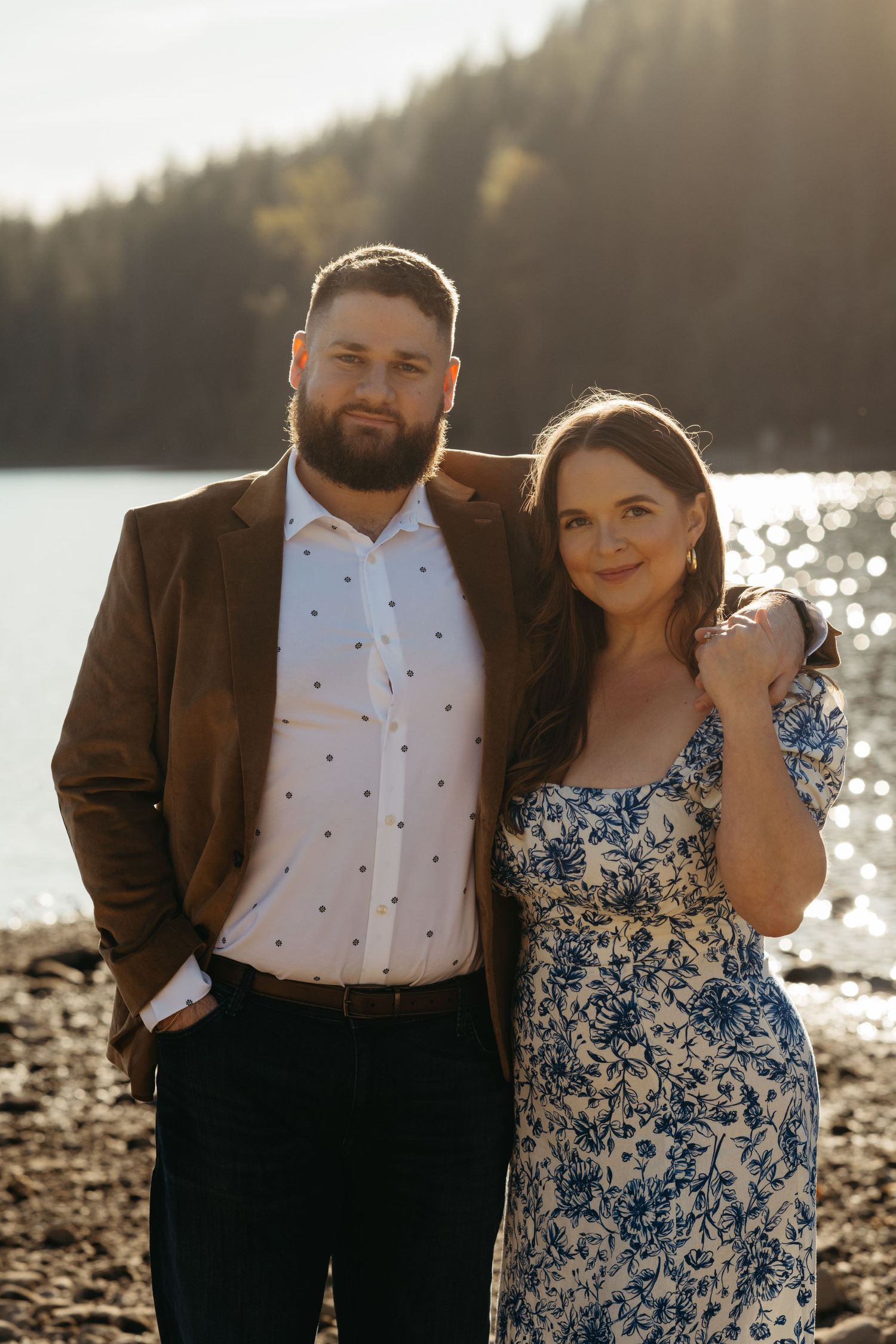 A couple poses together by a lake at sunset wearing coordinated formal attire.