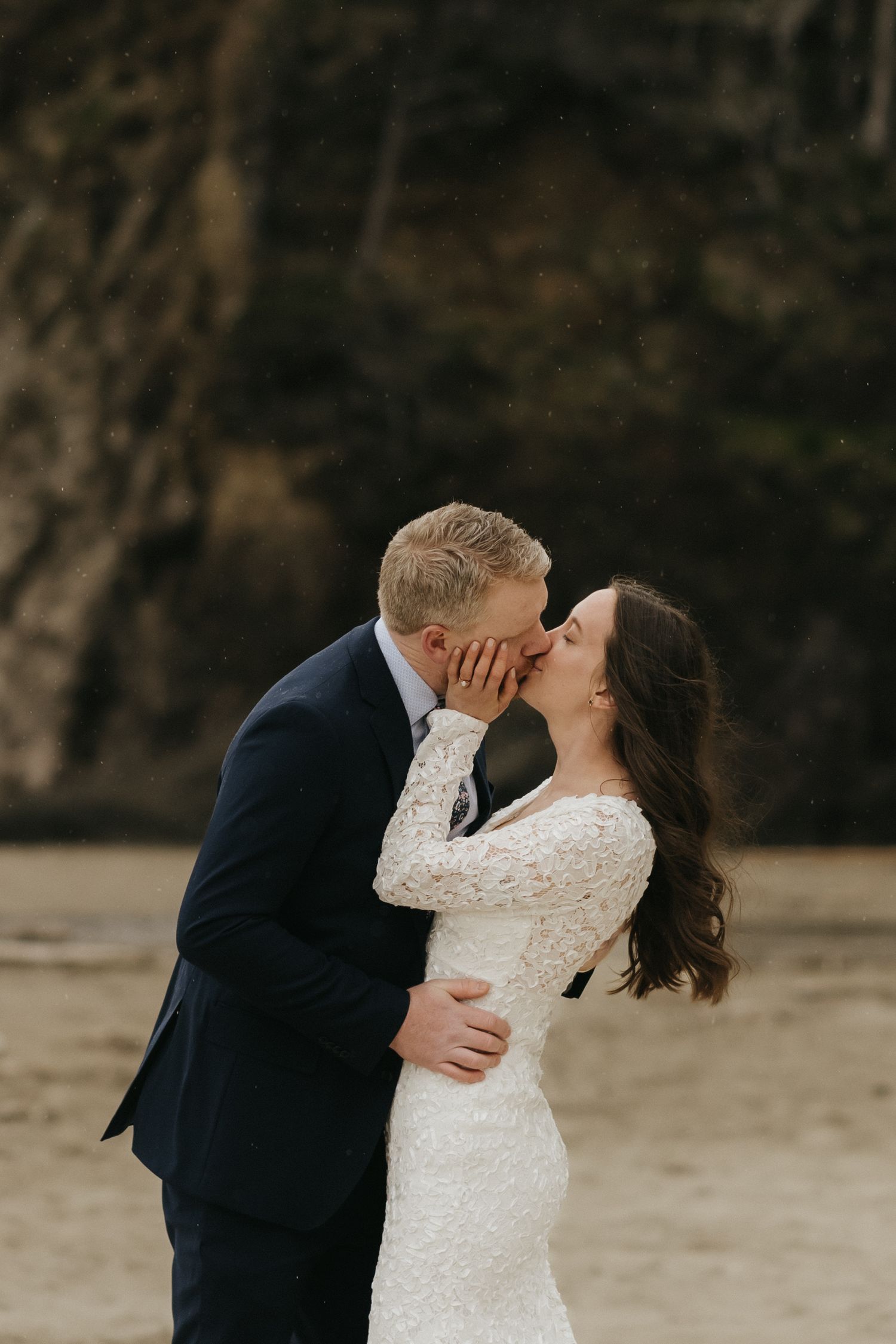 Intimate moment between newlyweds on a scenic beach with cliffs in the background.