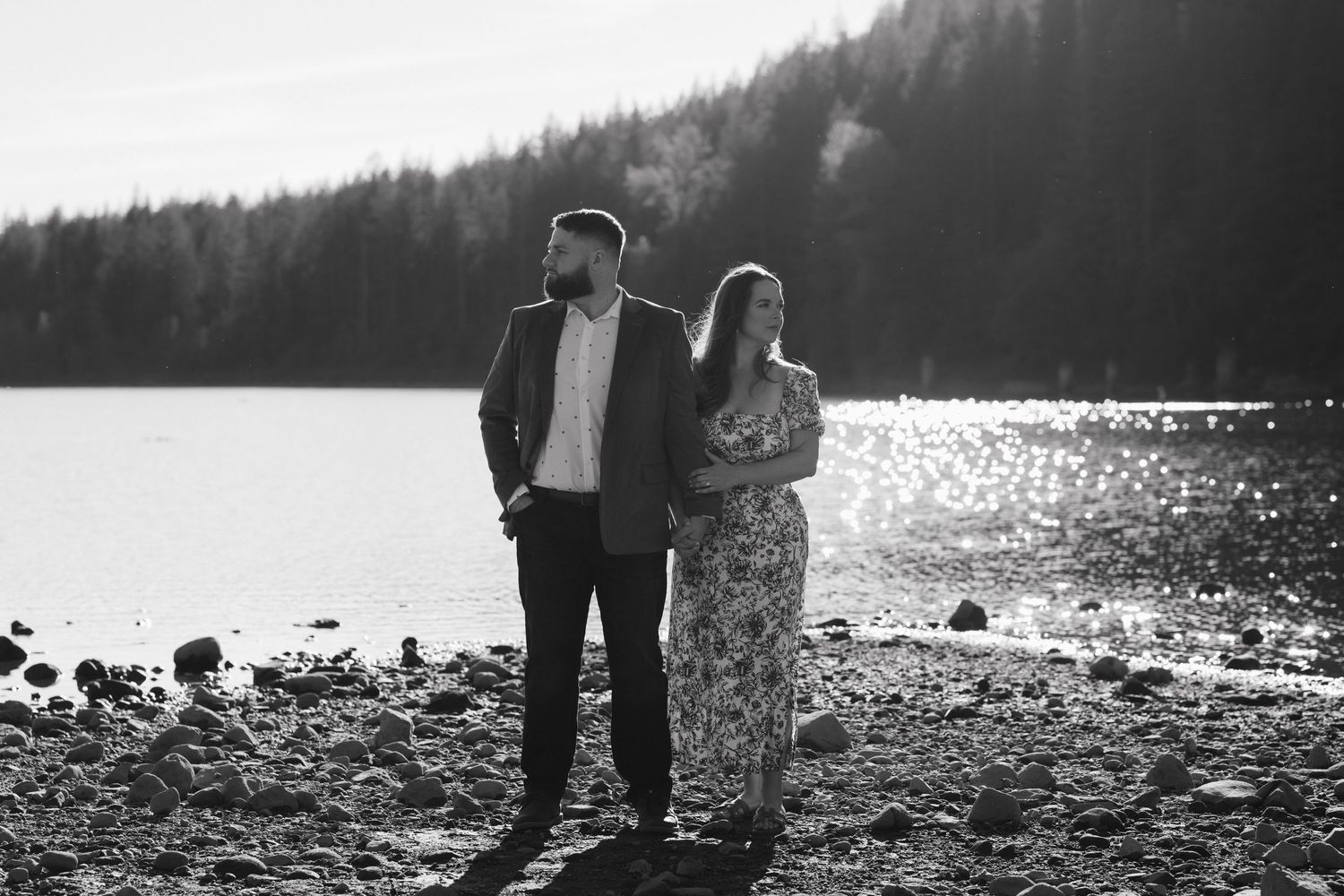 A black and white portrait of a couple standing together on a rocky lakeshore.