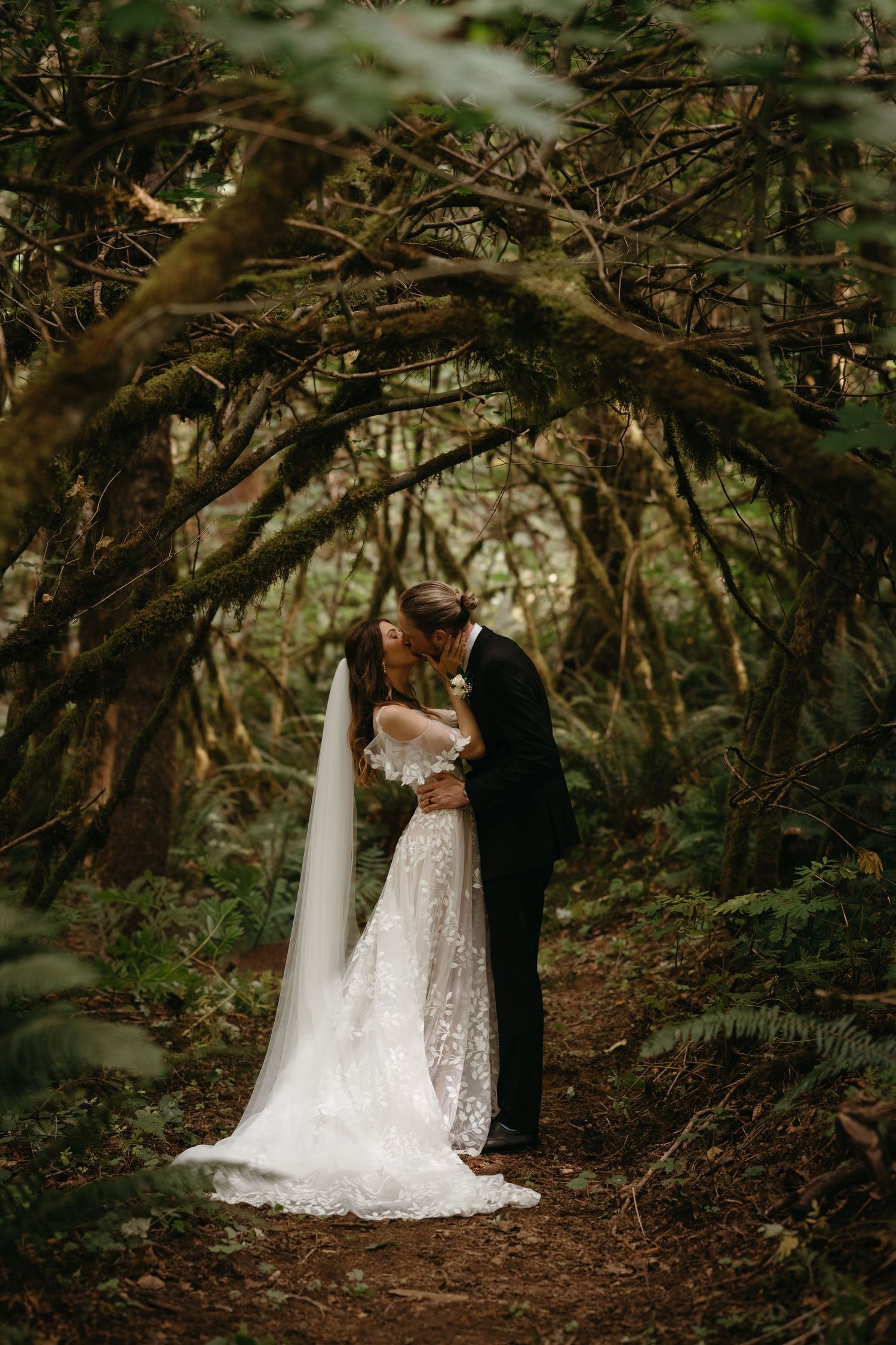Couple embraces under natural archway of twisted trees in enchanted forest setting.