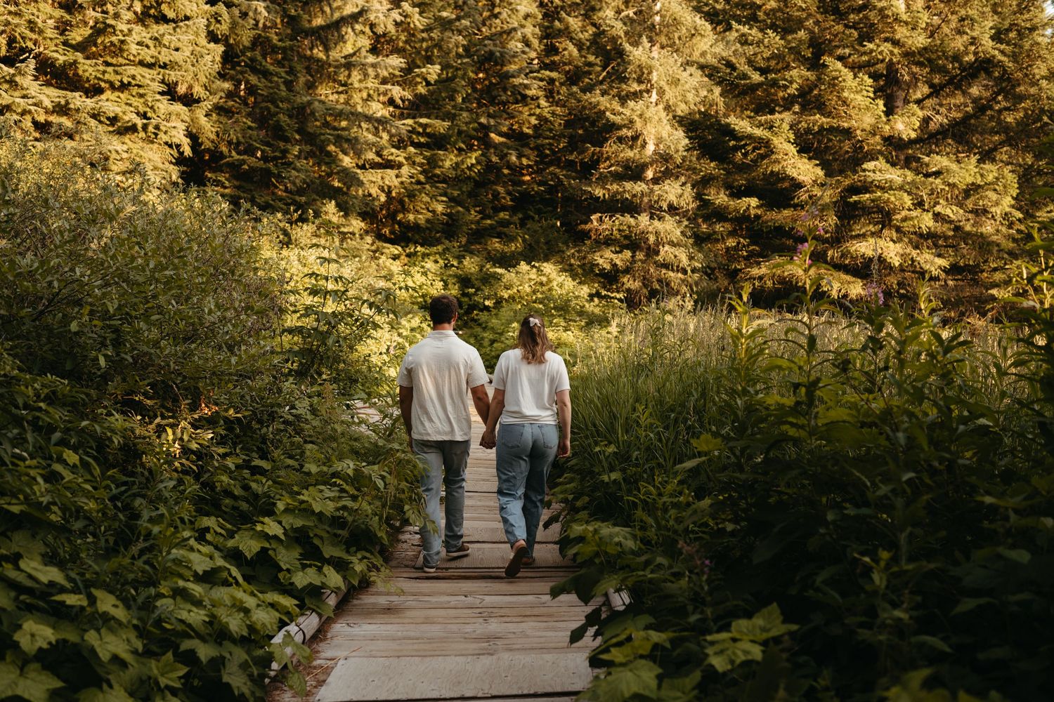 Couple walking hand in hand on wooden boardwalk through mountain wilderness.