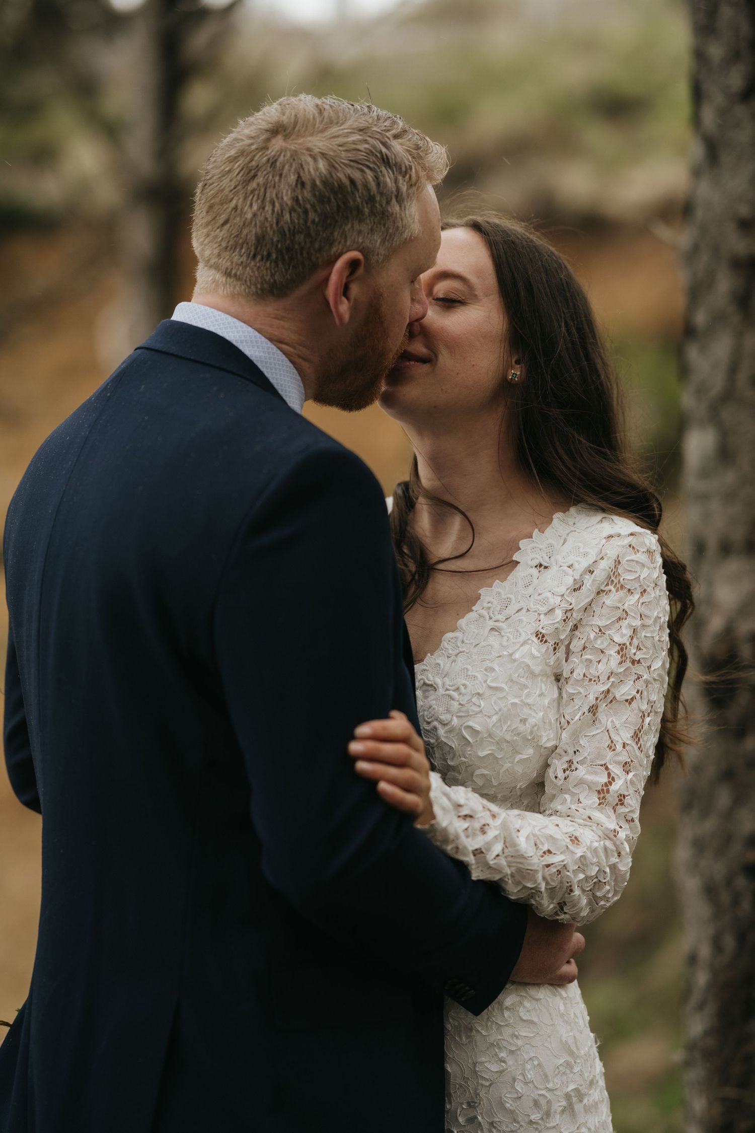 An intimate wedding portrait captured between trees during an outdoor ceremony.