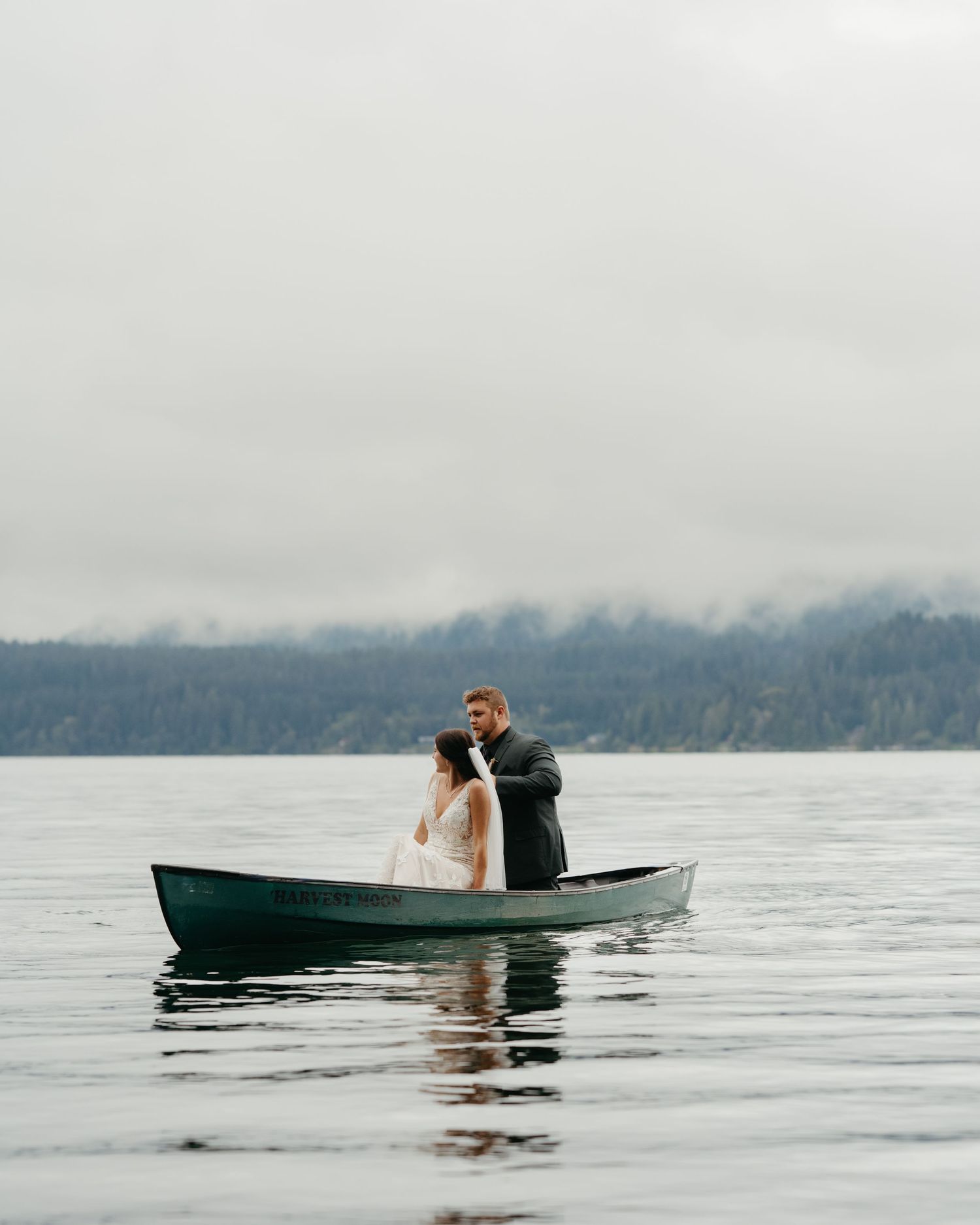 Bride and groom share romantic moment in canoe on misty lake.