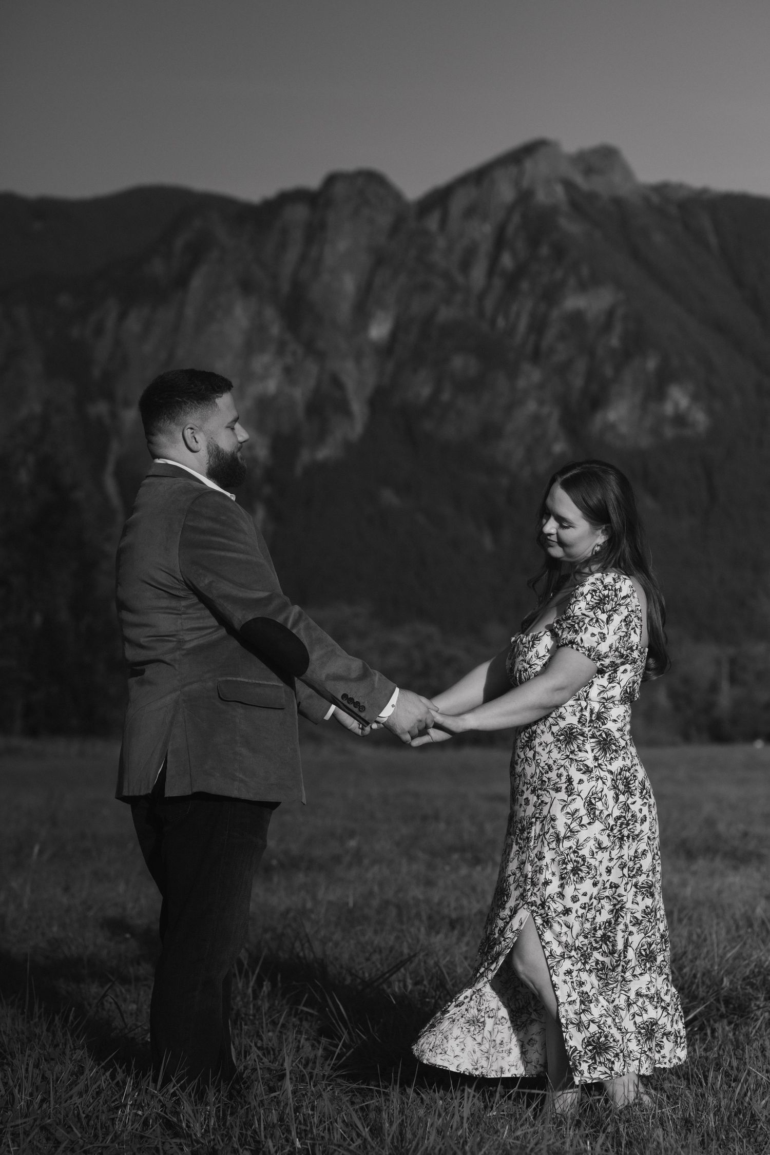 Black and white portrait of couple holding hands in mountain meadow with rugged peaks behind them.