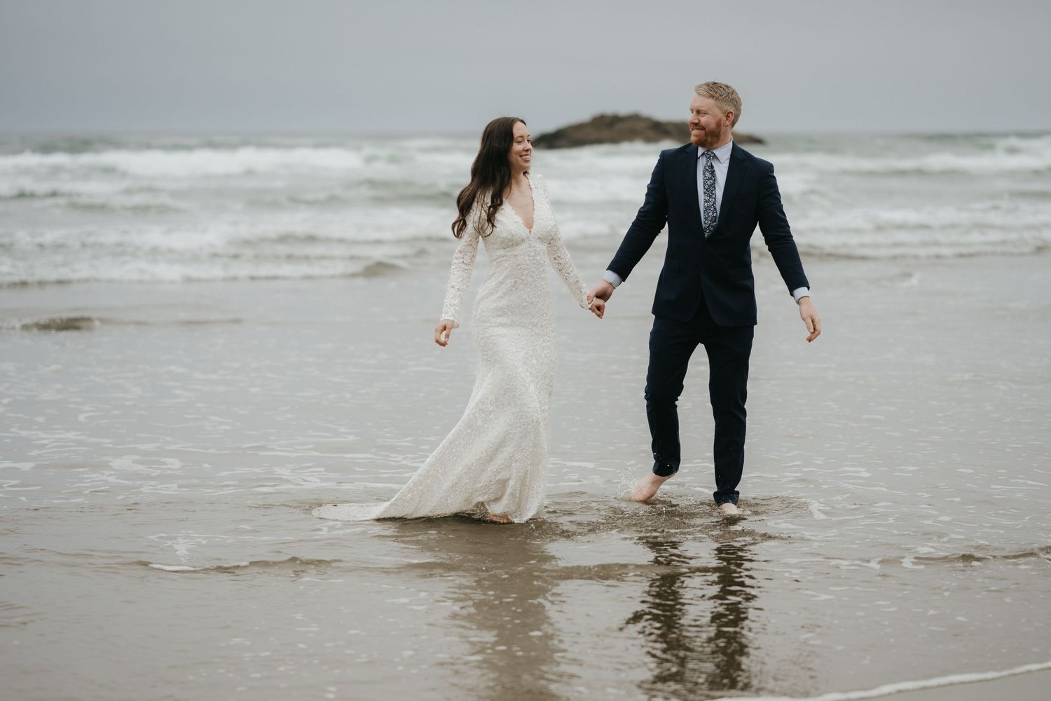 Couple playing in ocean waves during their beach wedding celebration.