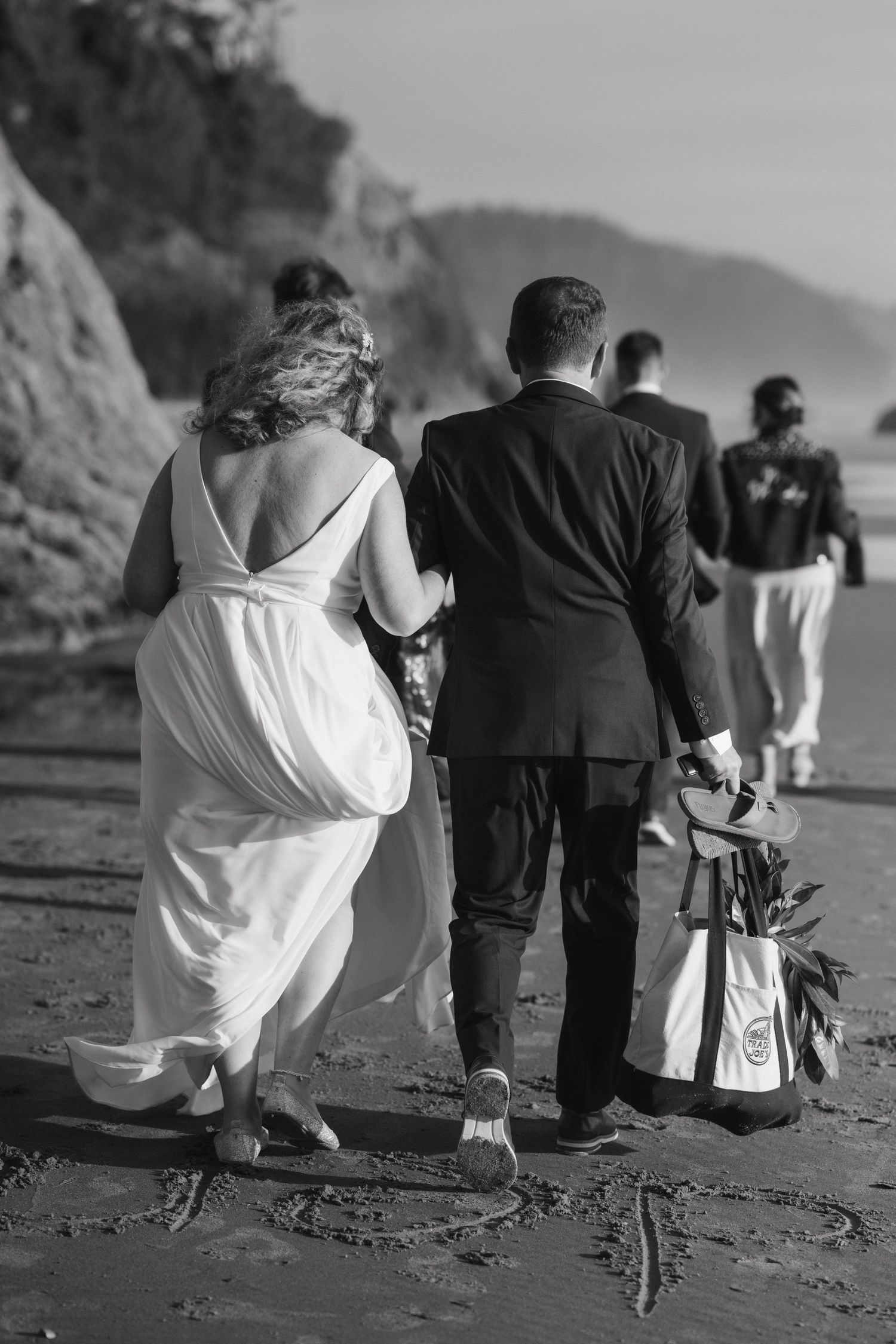 A wedding party walking along a rocky coastal beach path in black and white.