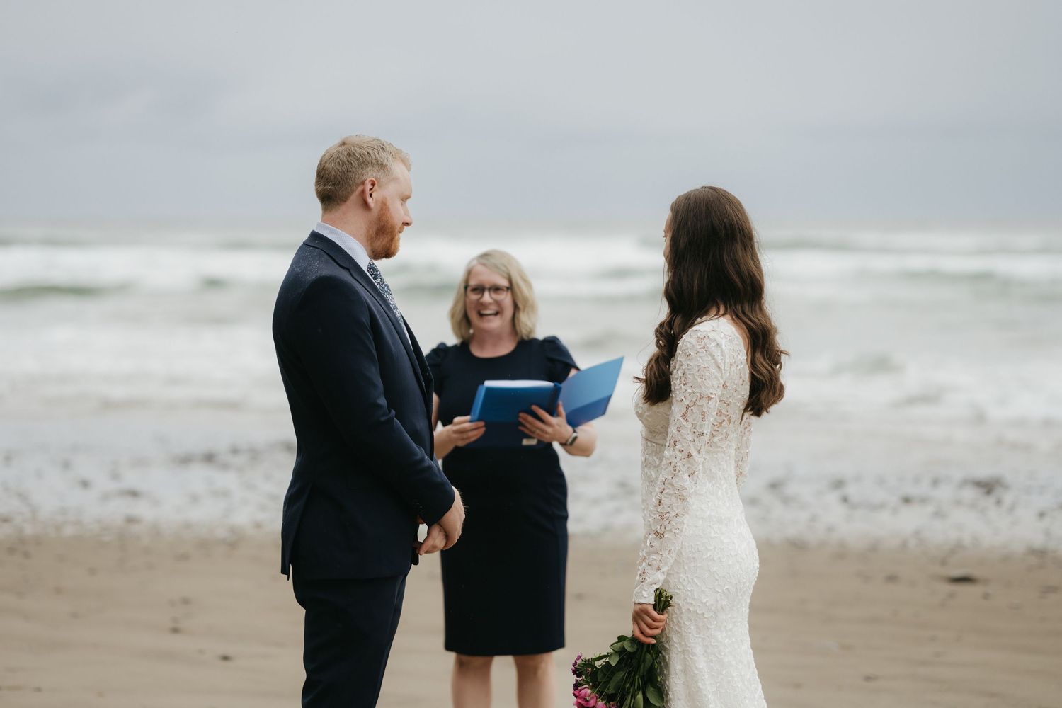 An intimate beach wedding ceremony with crashing waves and cloudy skies in the background.