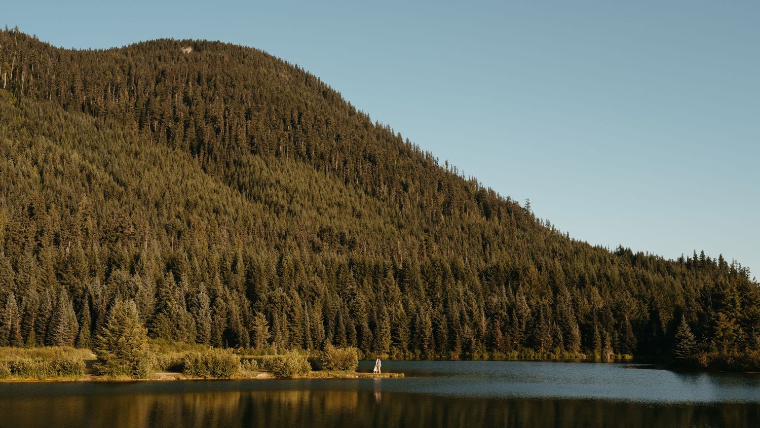 Serene mountain lake surrounded by evergreen forest slopes during golden hour.