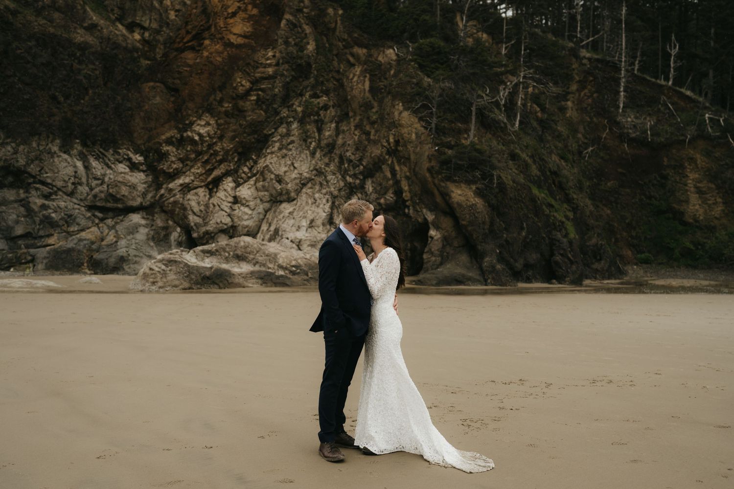 A romantic beach wedding ceremony with rocky cliffs in the background on a cloudy day.