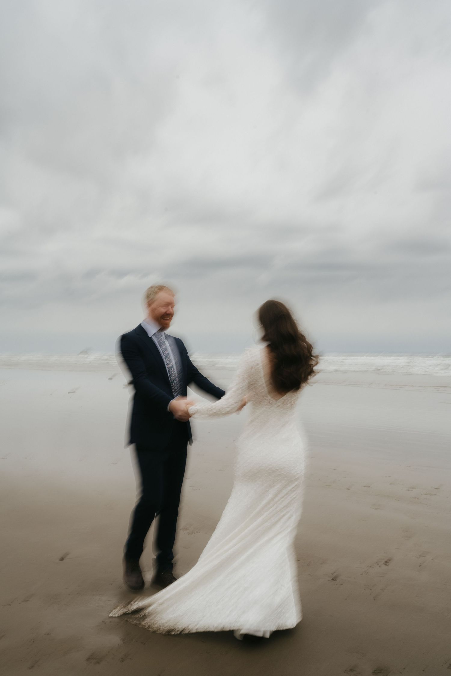 Romantic couple dancing together on a misty beach with cloudy skies in the background.